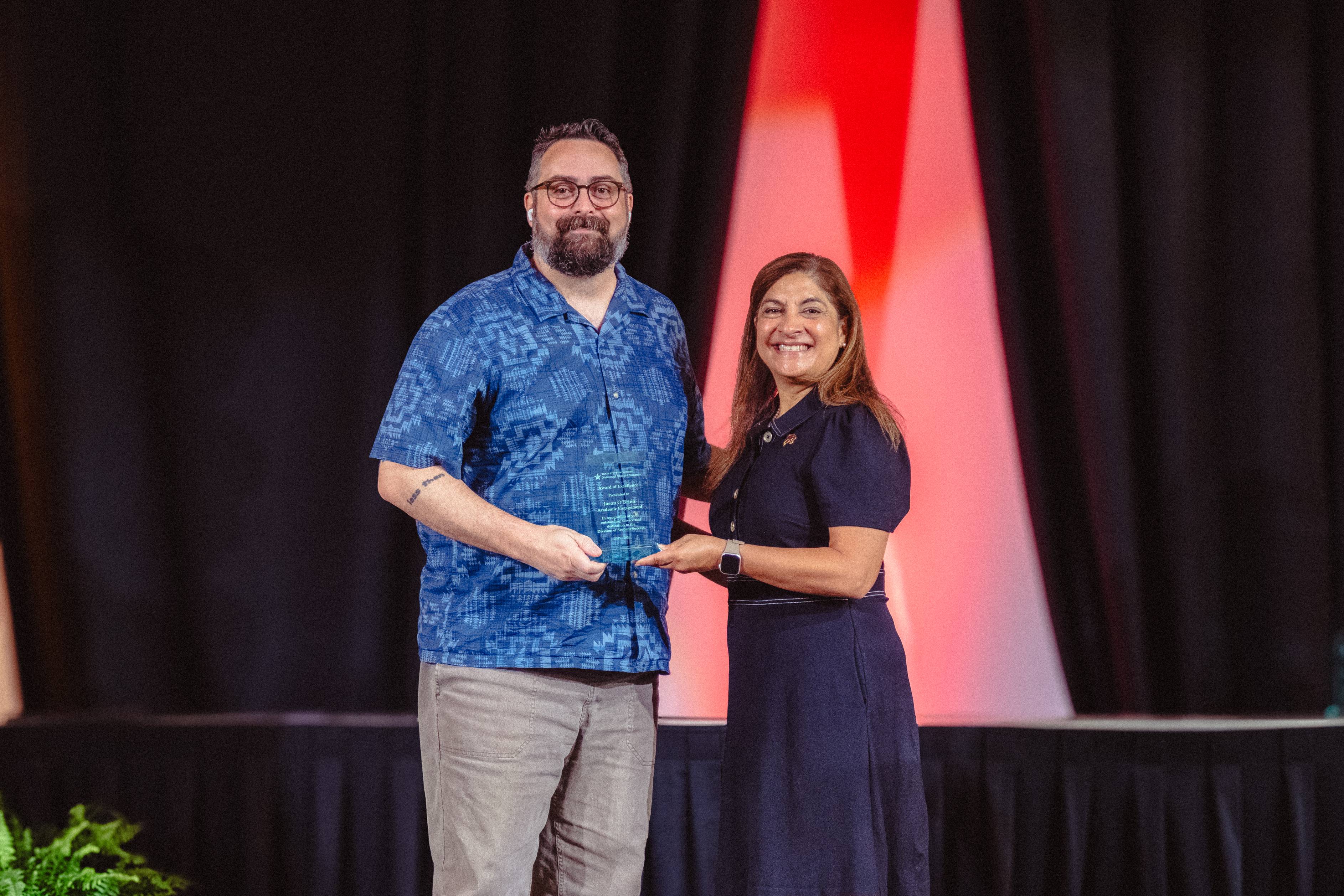 Jason O'Brien and Dr. Cynthia L. Hernandez Hold an award on stage 