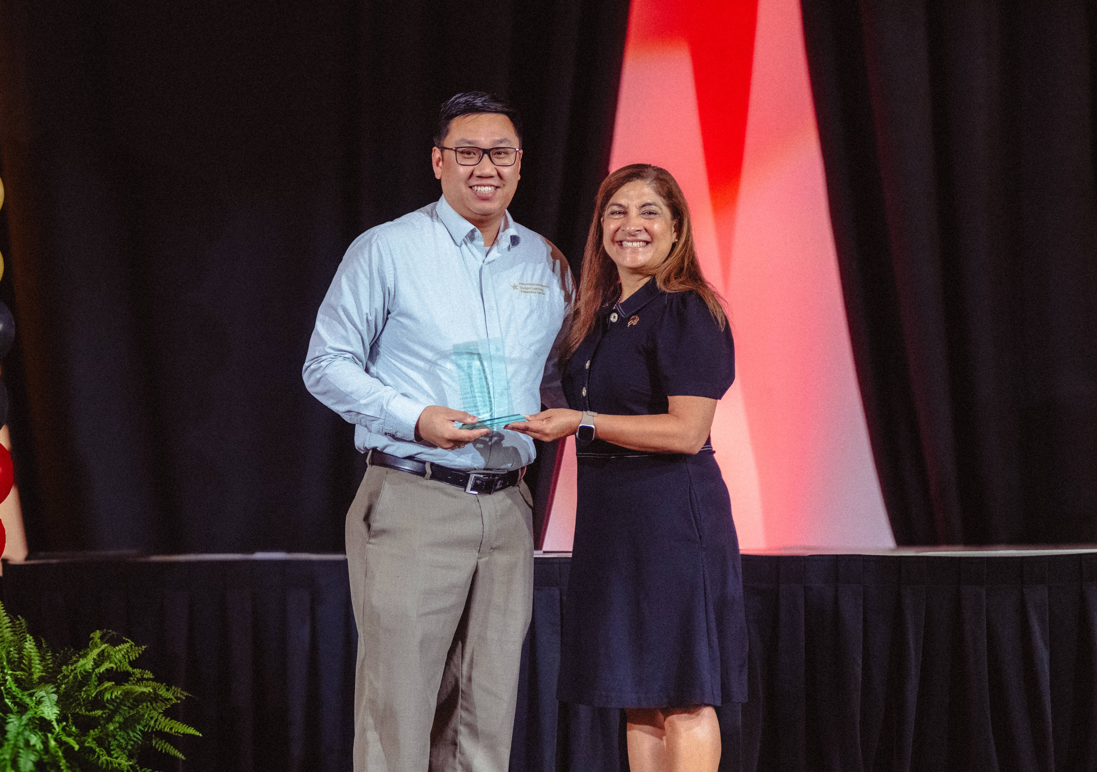 Dr. Tyler Laughlin and Dr. Cynthia L. Hernandez Hold an award on stage 