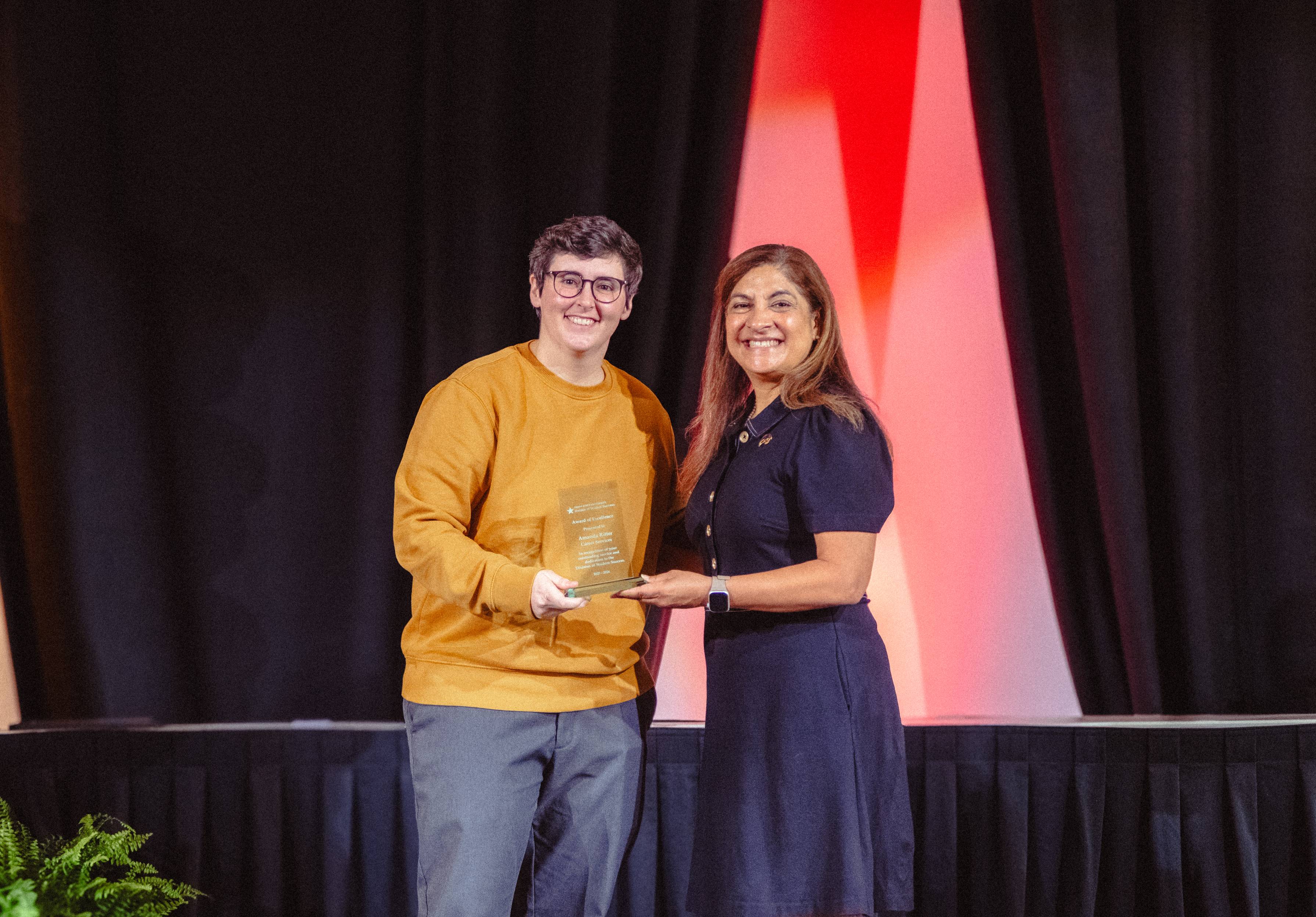 Amanda Ritter and Dr. Cynthia L. Hernandez Hold an award on stage 