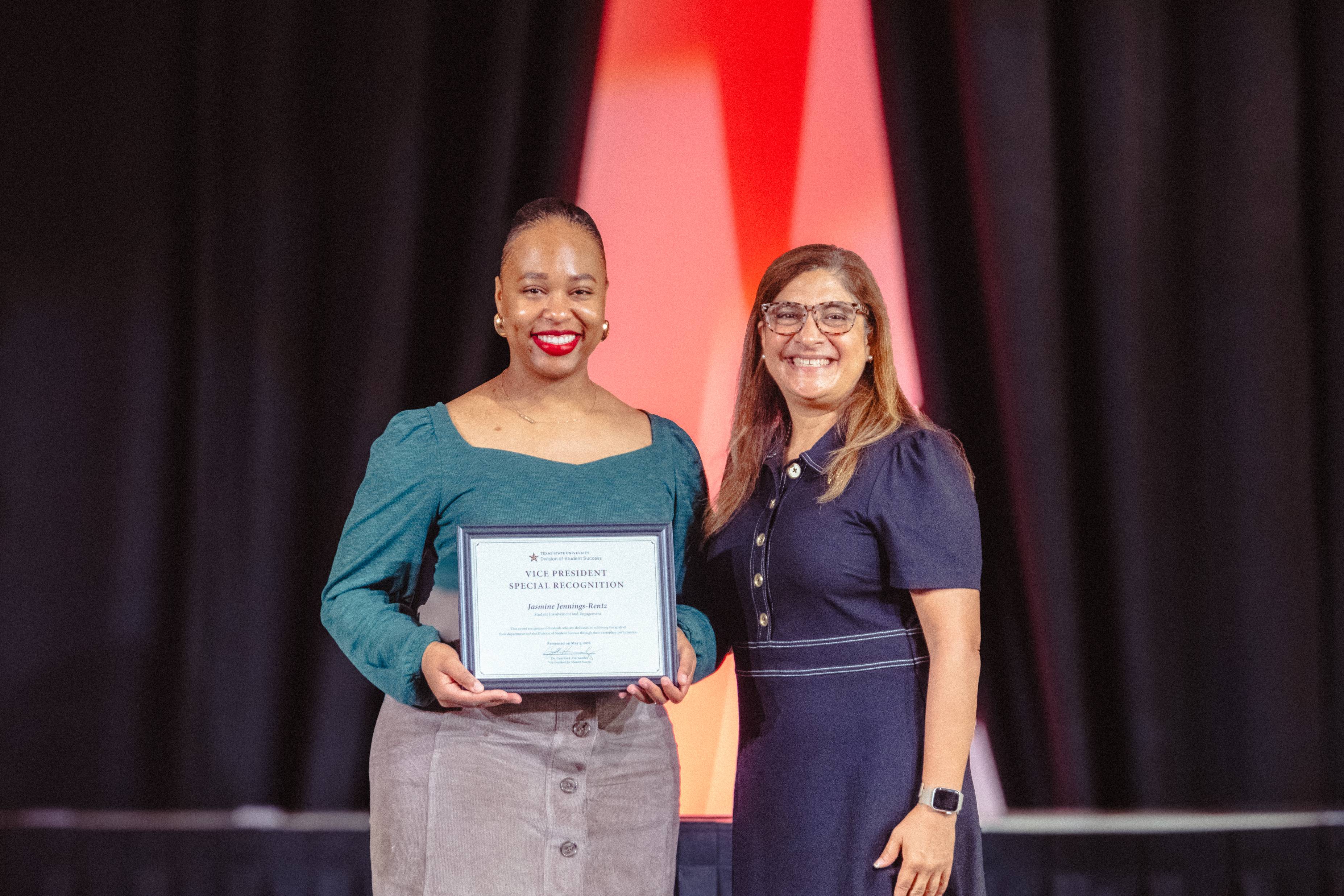 Dr. Cynthia L. Hernandez and Dr. Jasmine Jennings-Rentz on stage holding an award. 