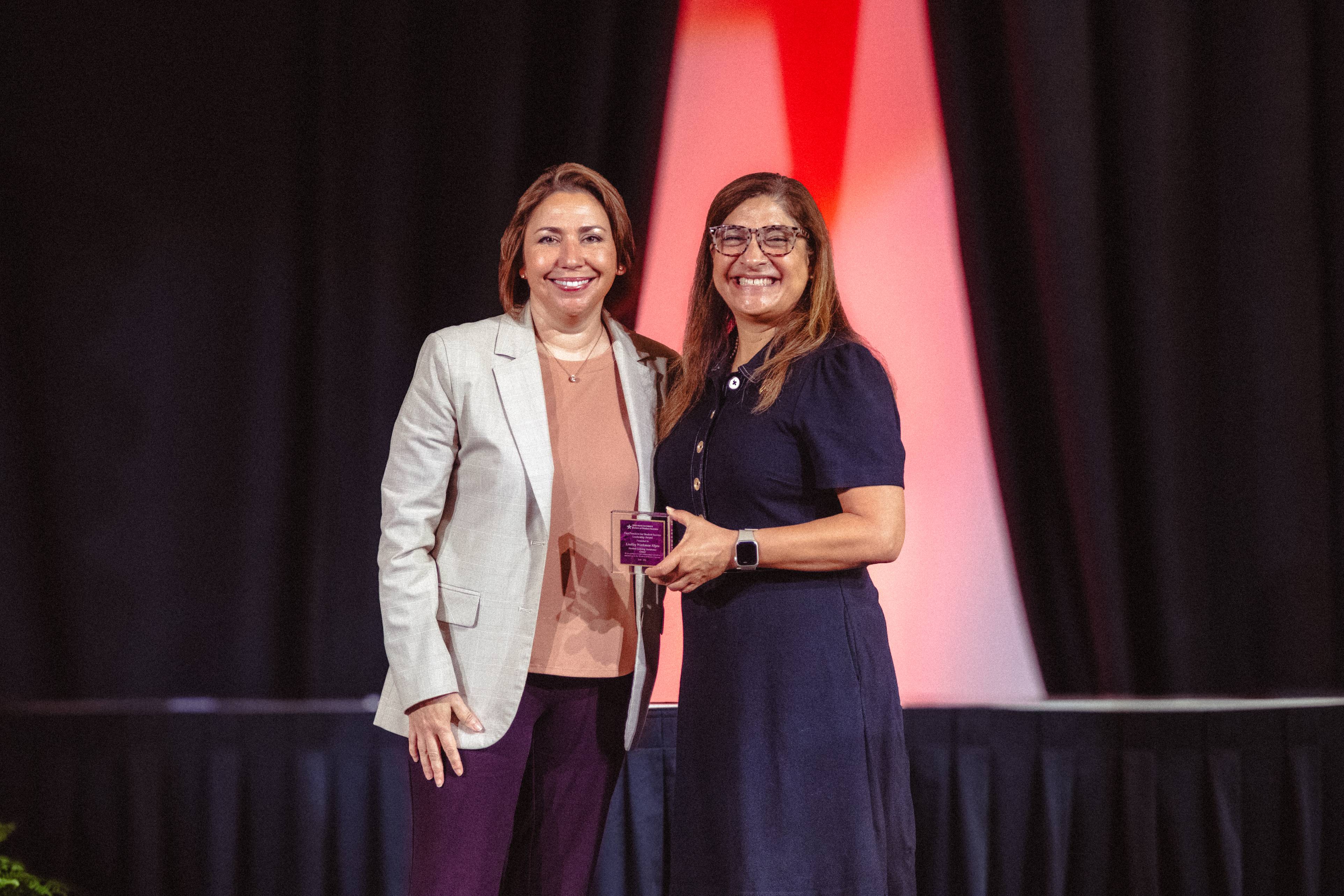 Dr. Cynthia L. Hernandez and Lindley Workman Alyea on stage holding an award. 