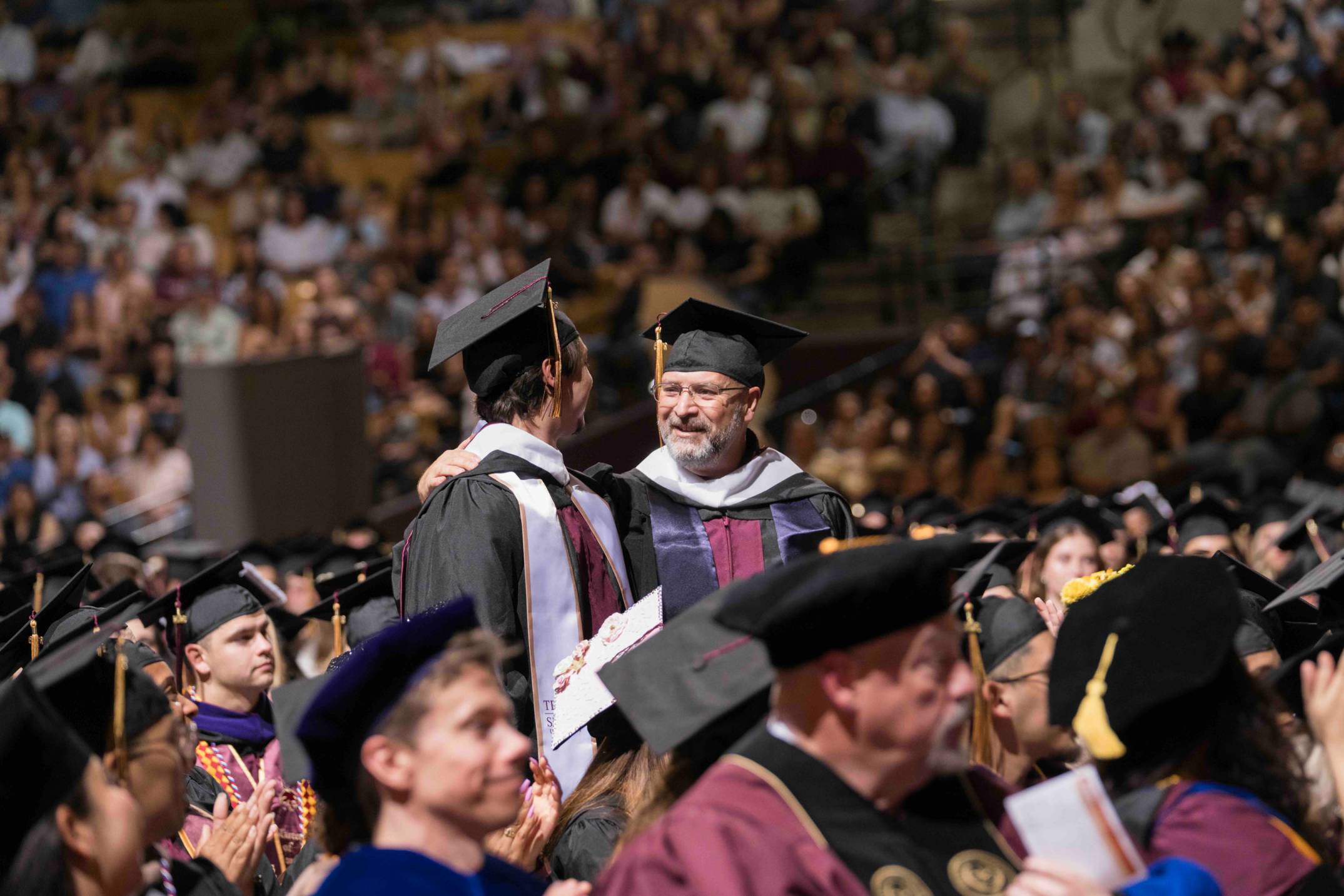two men look at each other ina. sea of cap and gowns