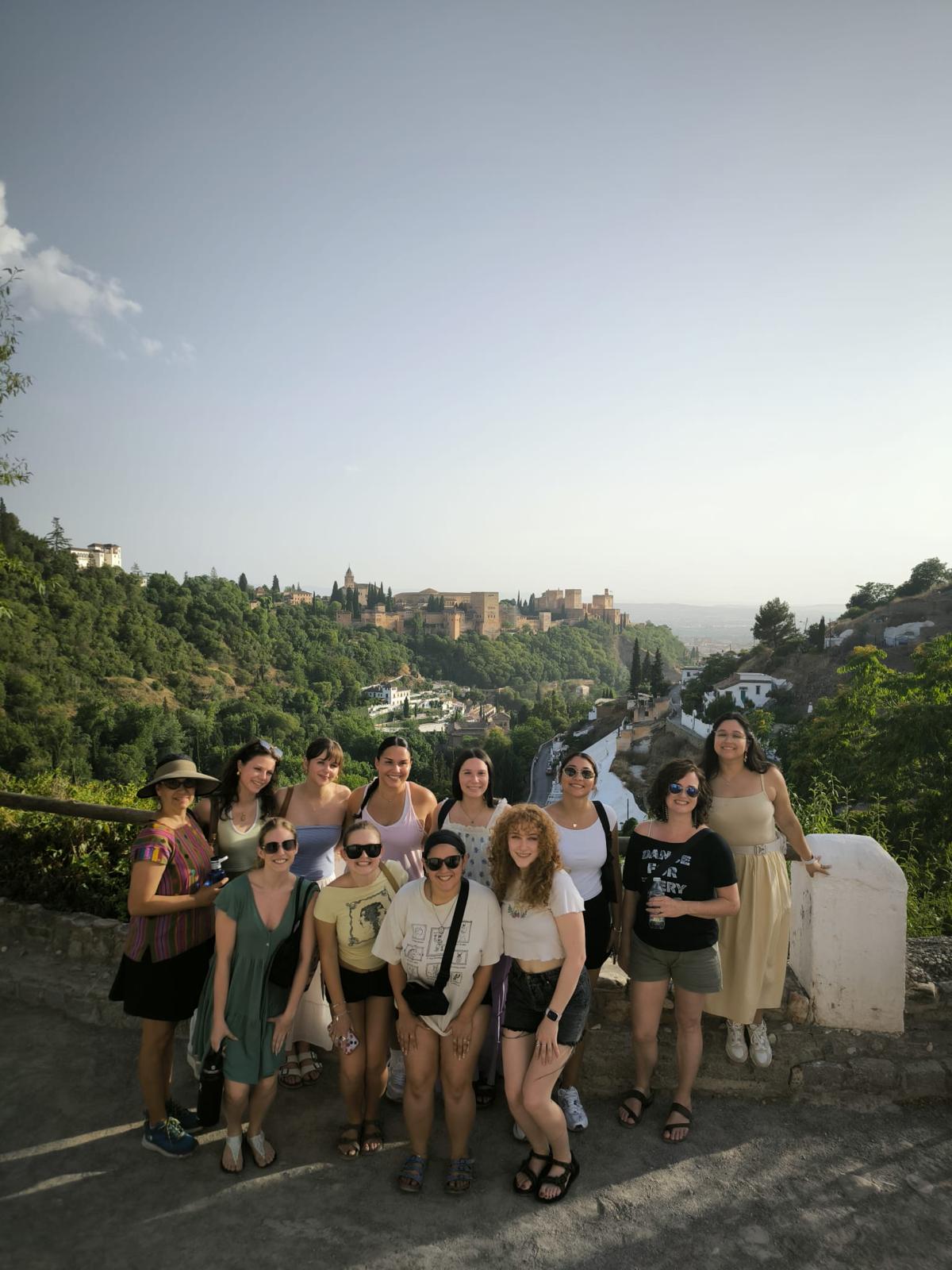 A group of dance study abroad students standing and smiling together on an outdoor path with the scenic hills and historic architecture of Granada, Spain, in the background.