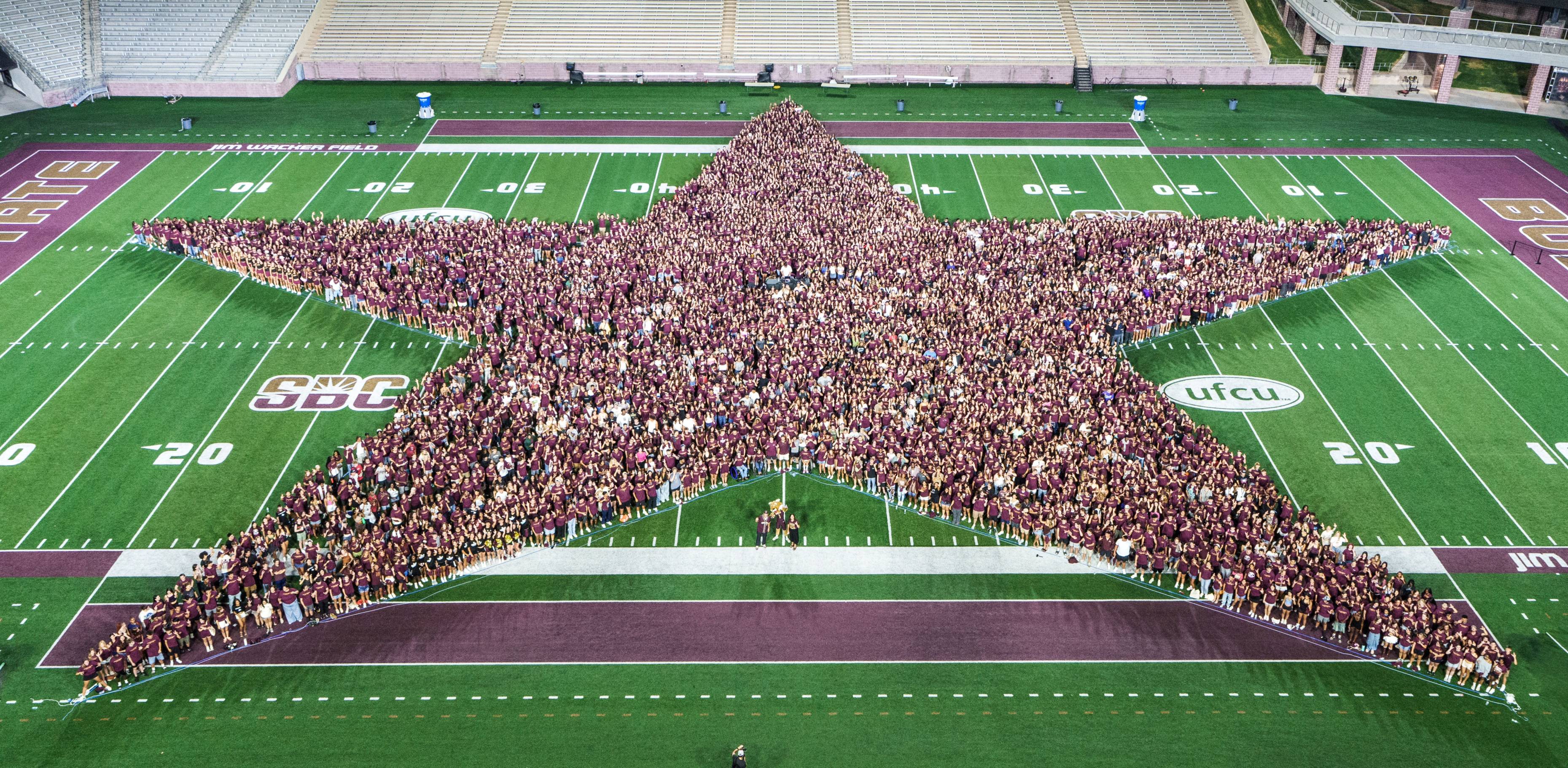 students standing in a star formation on a football field 