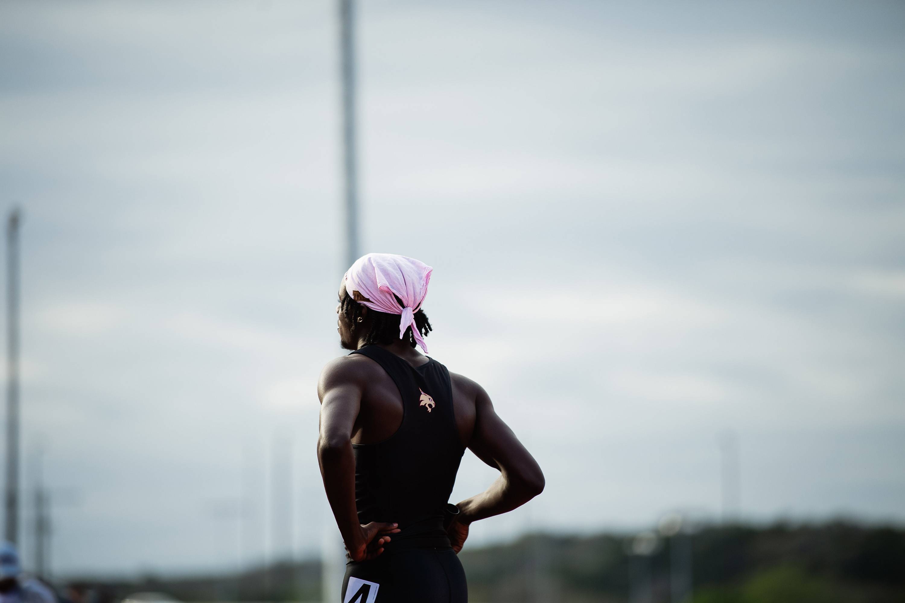 The back of Ja’Shaun Lloyd standing outside wearing a pink bandana and a black tank top with a gold bobcat logo on it.