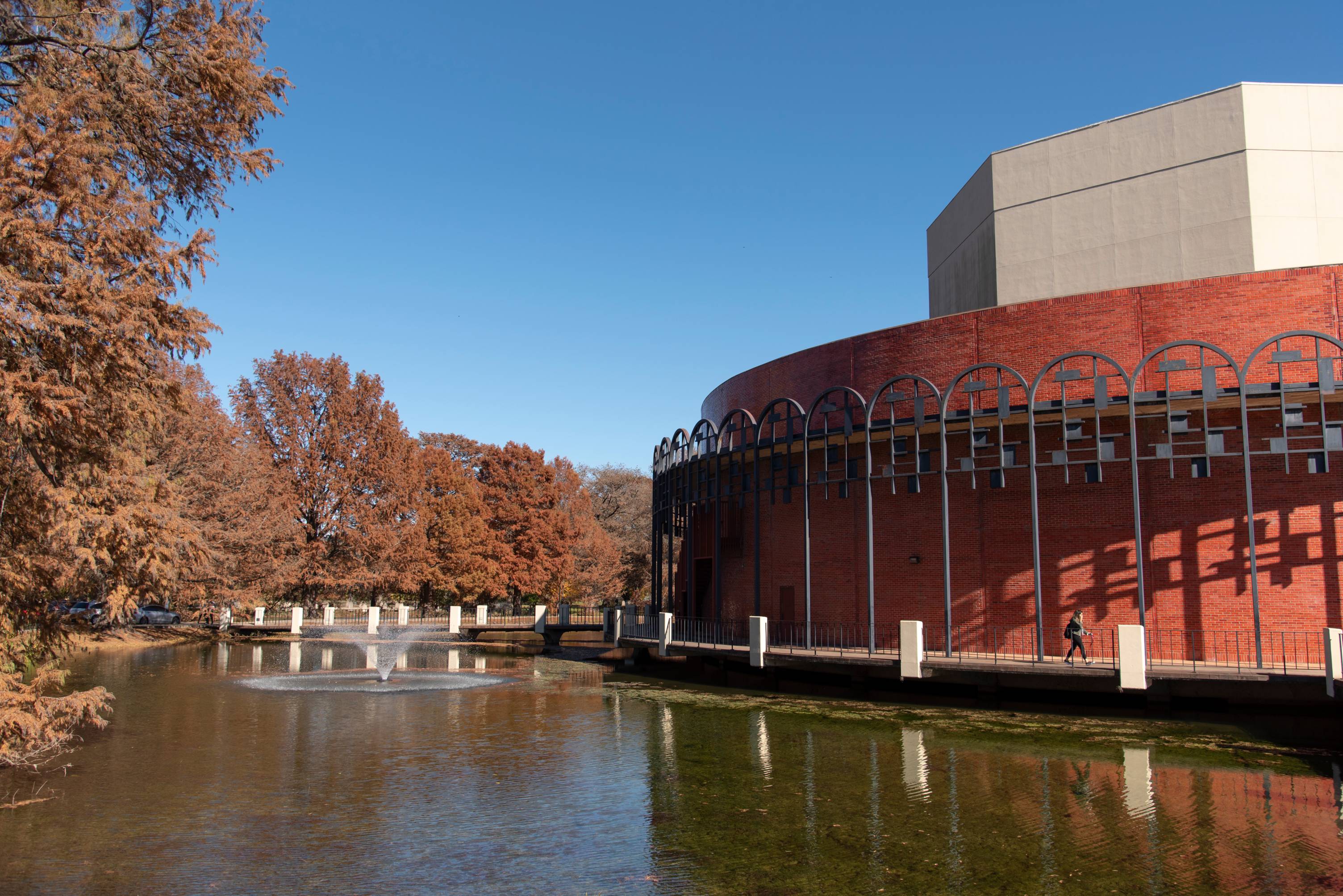 The Texas State University Theatre Center building standing next to the scenic moat lined with autumn trees.