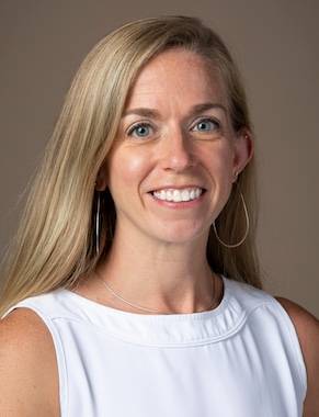Studio headshot of Sarah Maines smiling, featuring blonde hair and wearing a sleeveless white high-neck blouse against a neutral grey background.