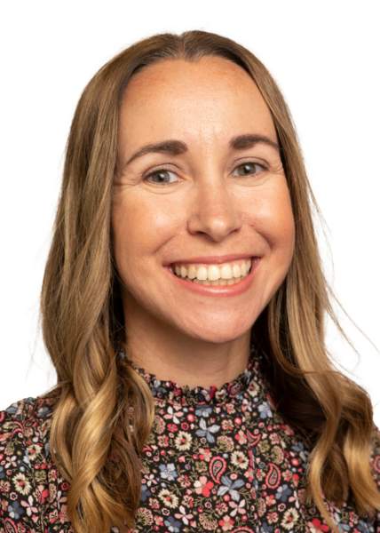 Studio headshot of Vlasta Silhavy smiling, with long wavy light brown hair and wearing a high-neck dark floral pattern blouse against a neutral background.