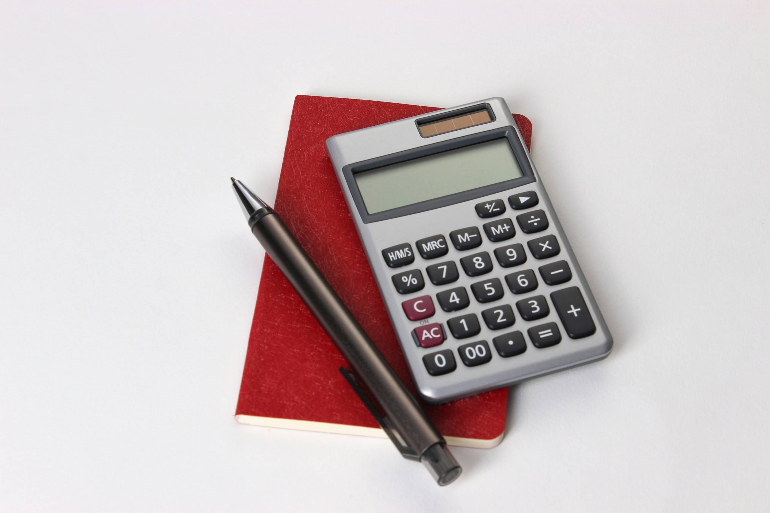 Calculator on top of a red notebook with a black pen.