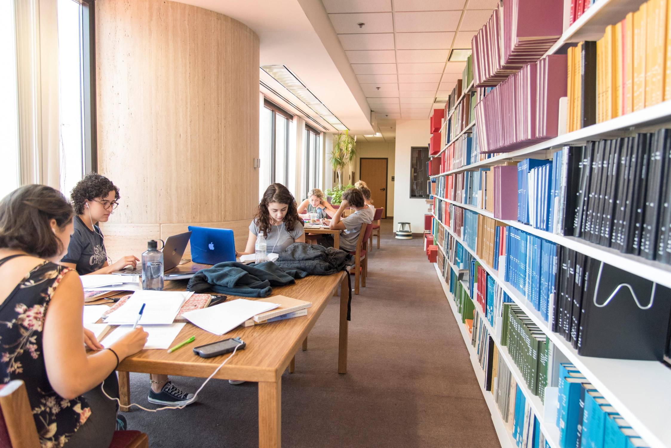 people studying at wooden desk next to large bookcases in library
