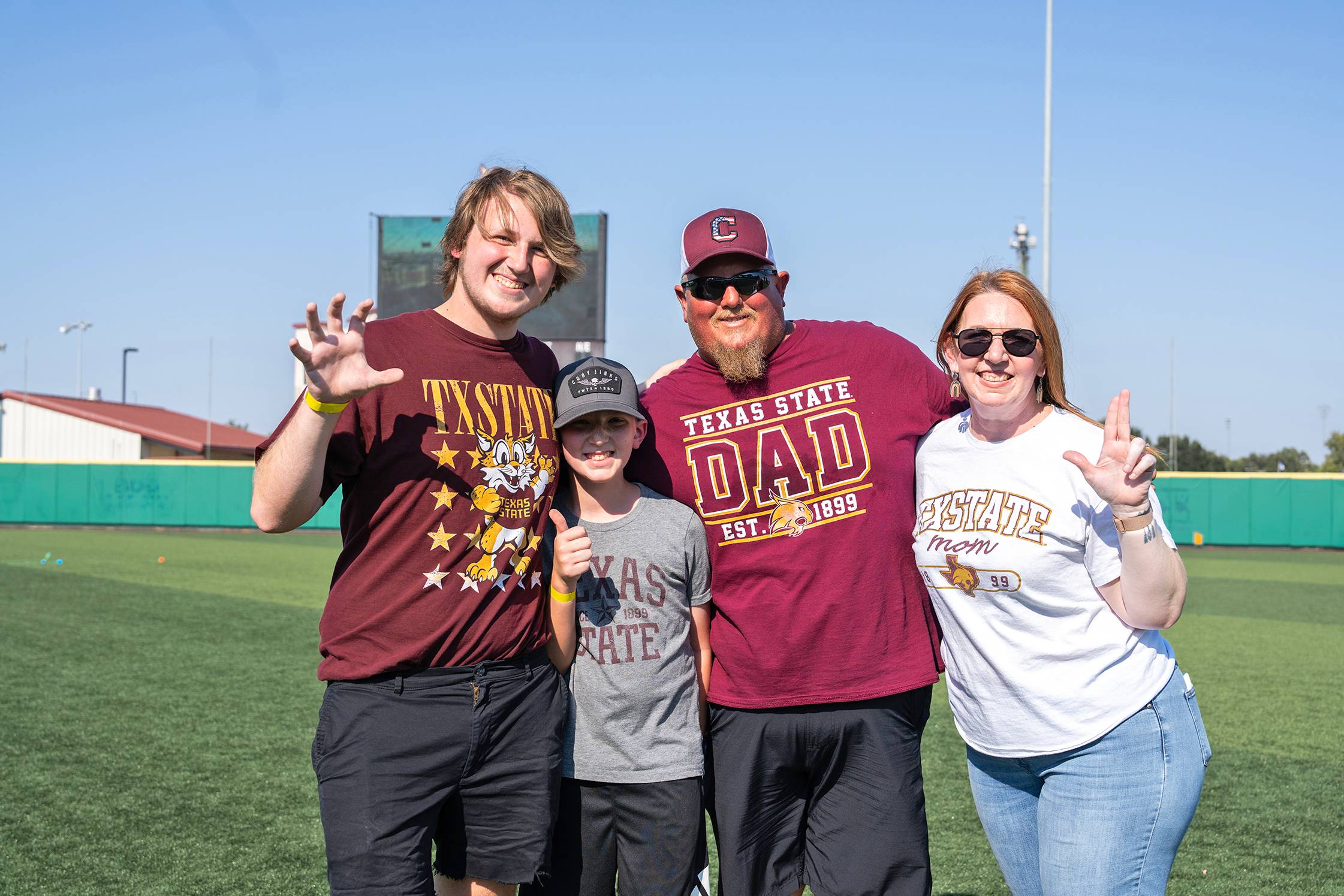 A student with their parents and sibling pose on the baseball field
