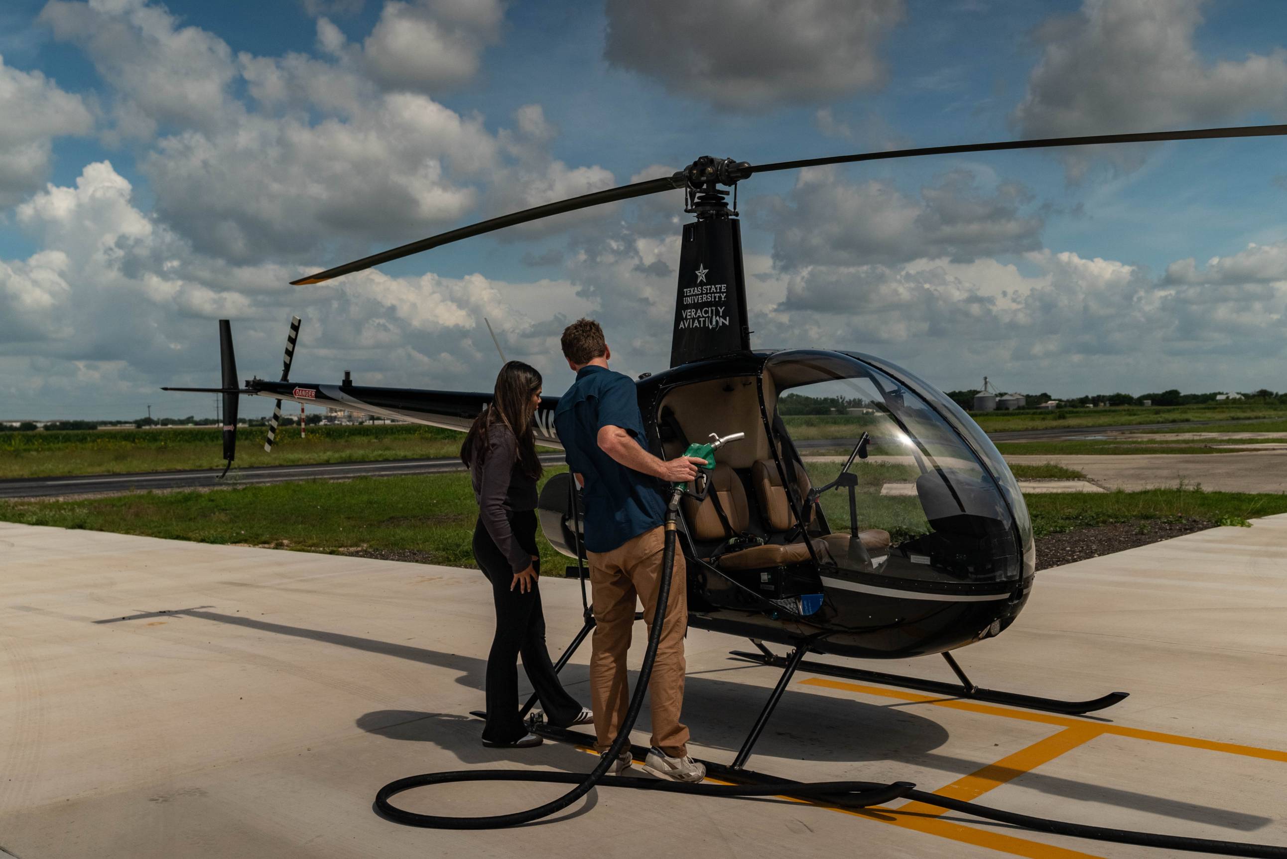 two people fueling up small black helicopter