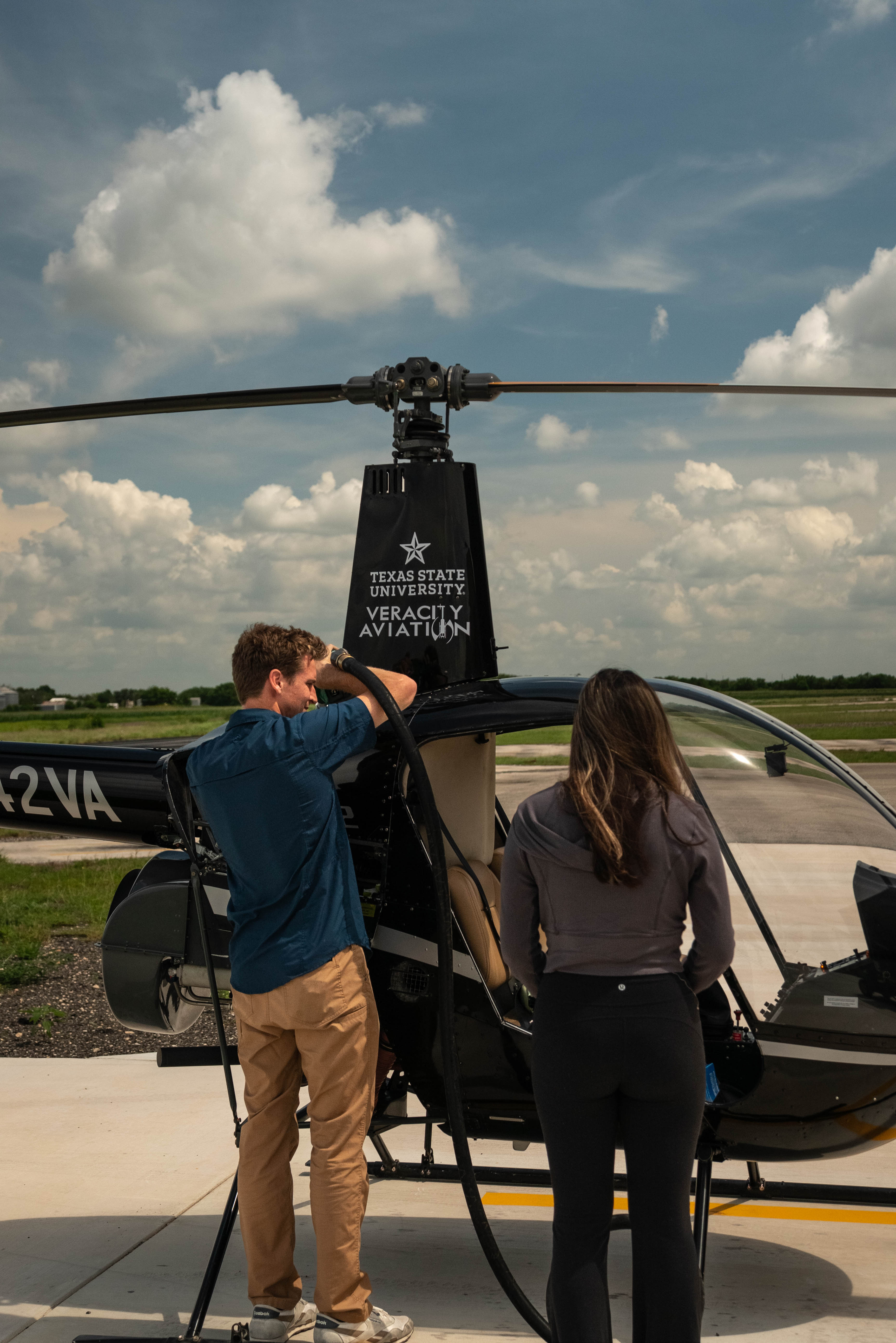 man fueling up helicopter while woman looks into the cockpit