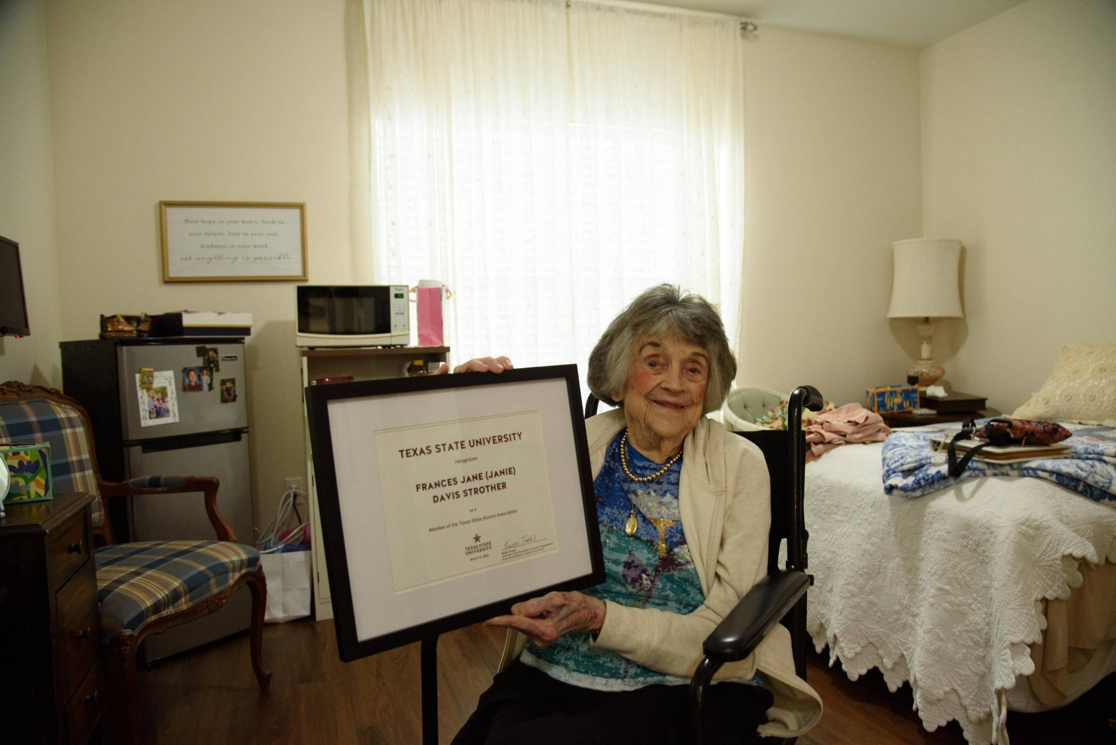 elderly woman holding up a certificate in bedroom
