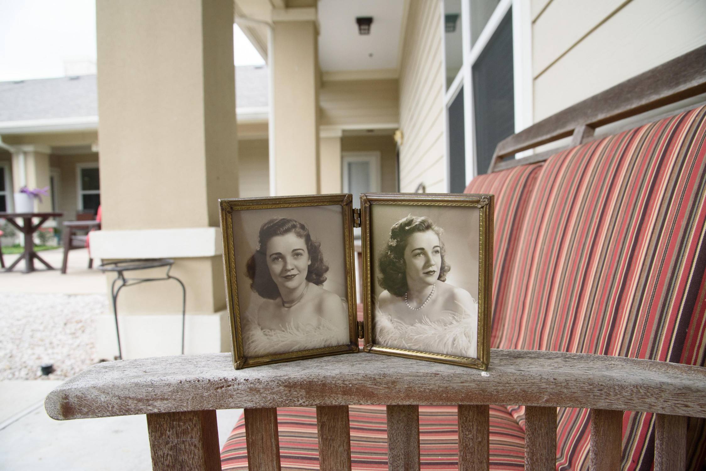 two old black and white photos of woman from the 1940s in a frame. it is sitting on the arm of an outdoor couch