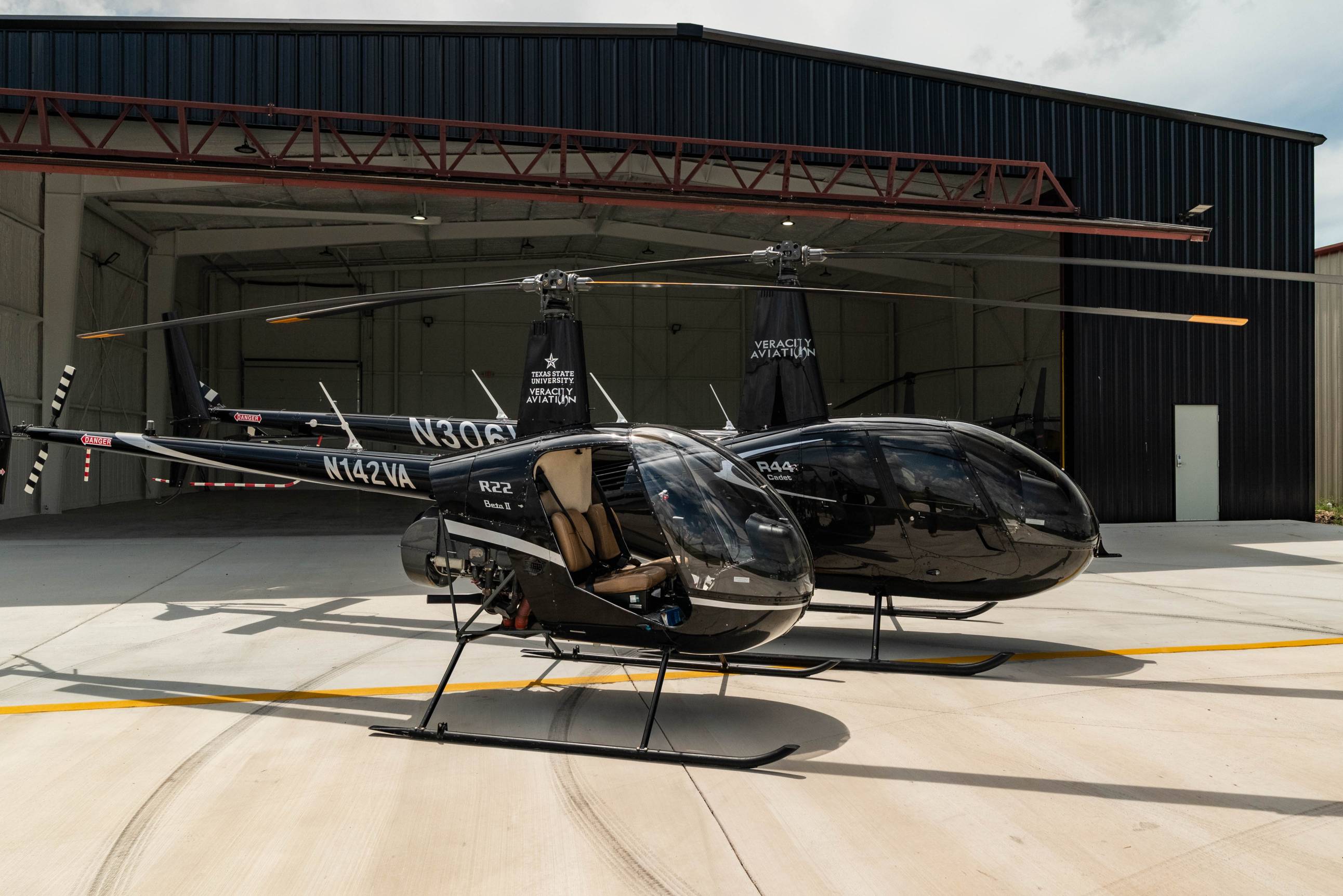 Two black helicopters outside of a hangar