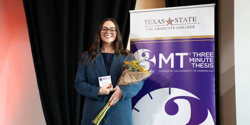 Cassandra M. Swanson standing next to a 3MT sign holding her name tag and runner-up announcement