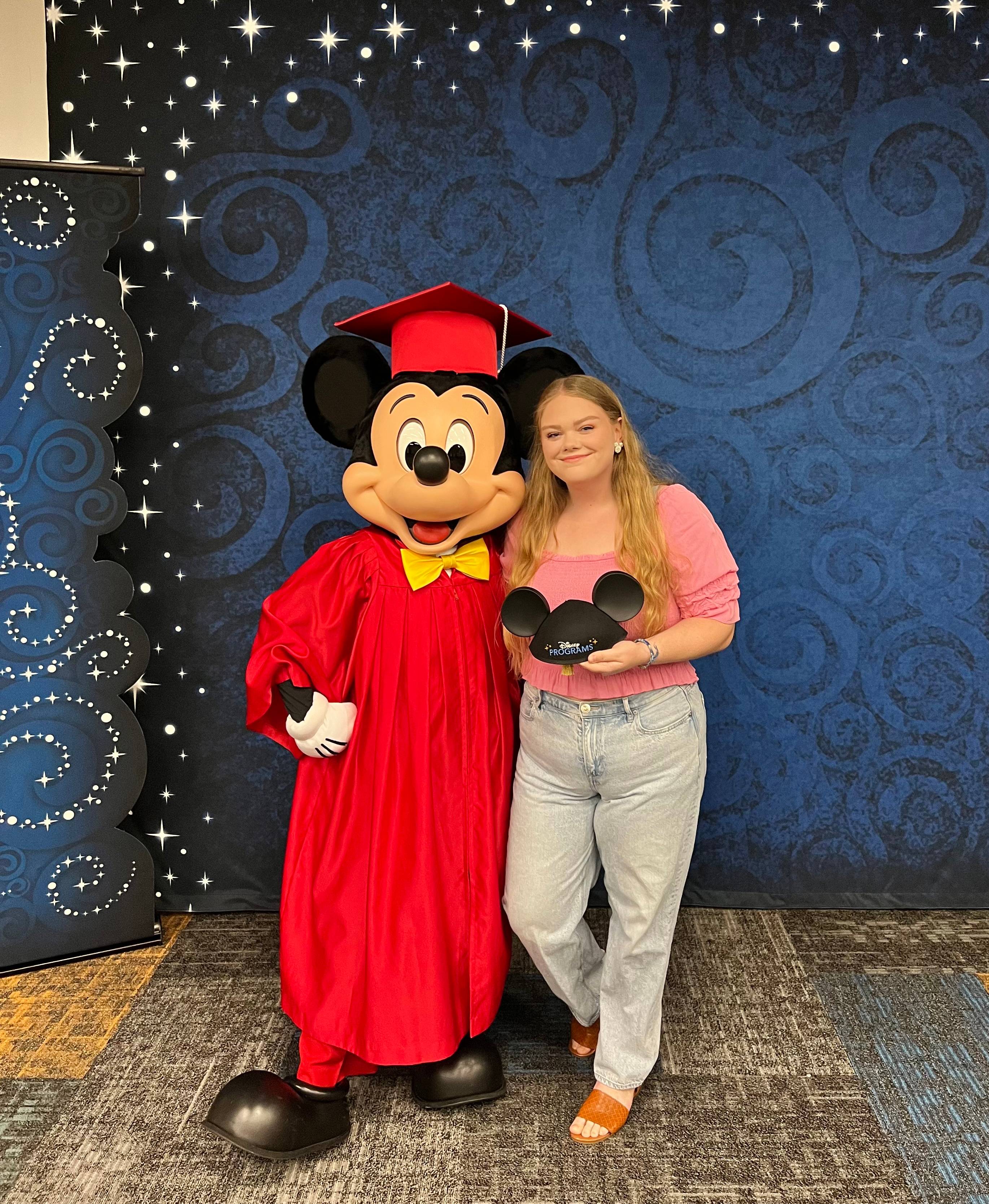 woman poses with mickey mouse character in graduation gown