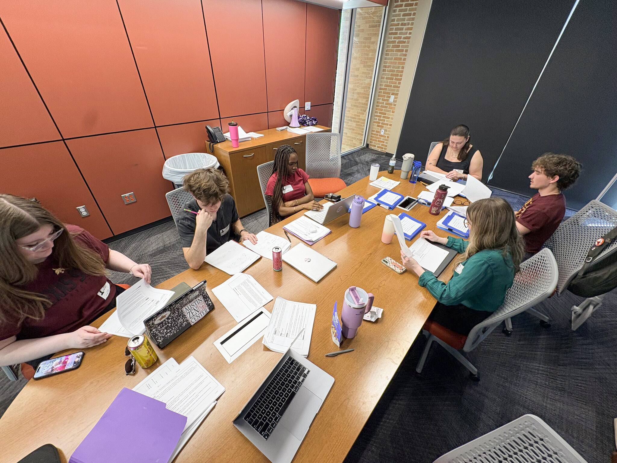 students sitting around wooden table looking at papers and laptops