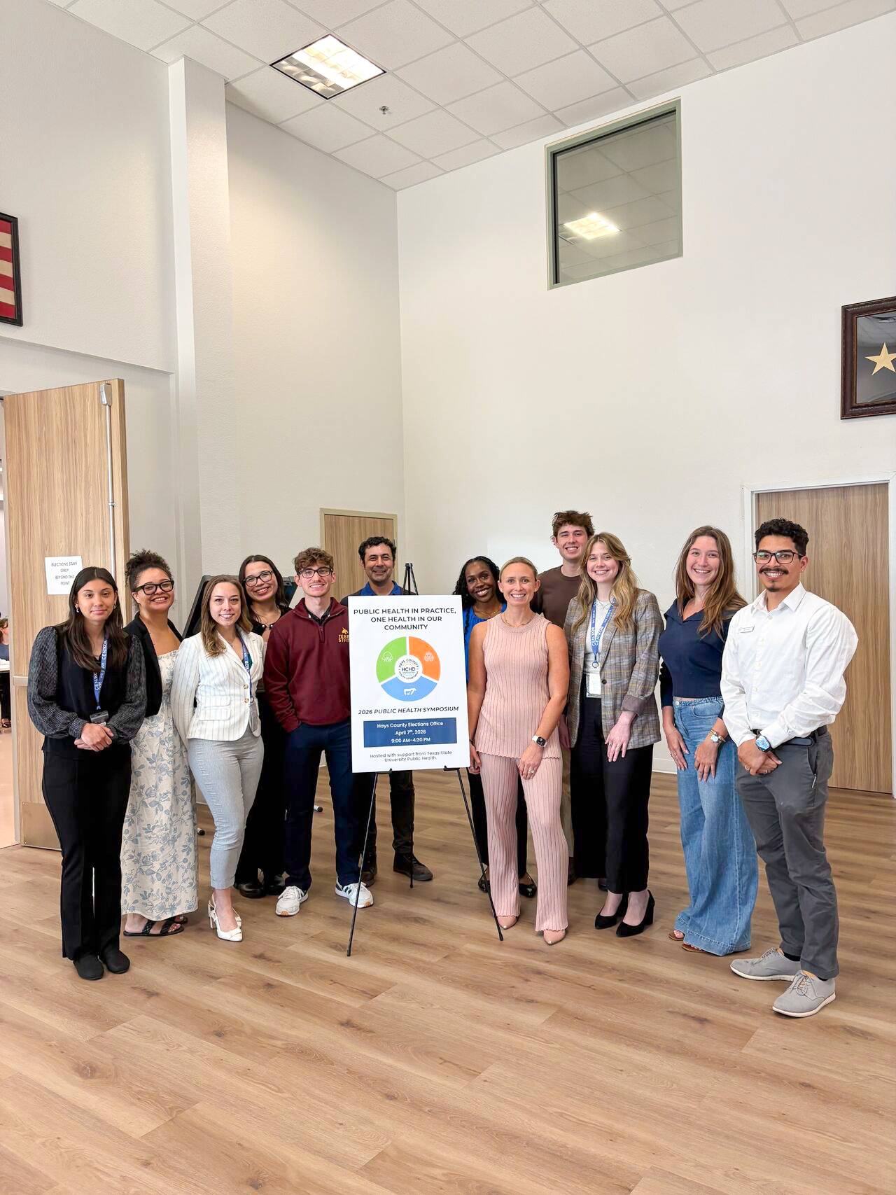 large group of faculty members and students pose next to a presentation on an easel