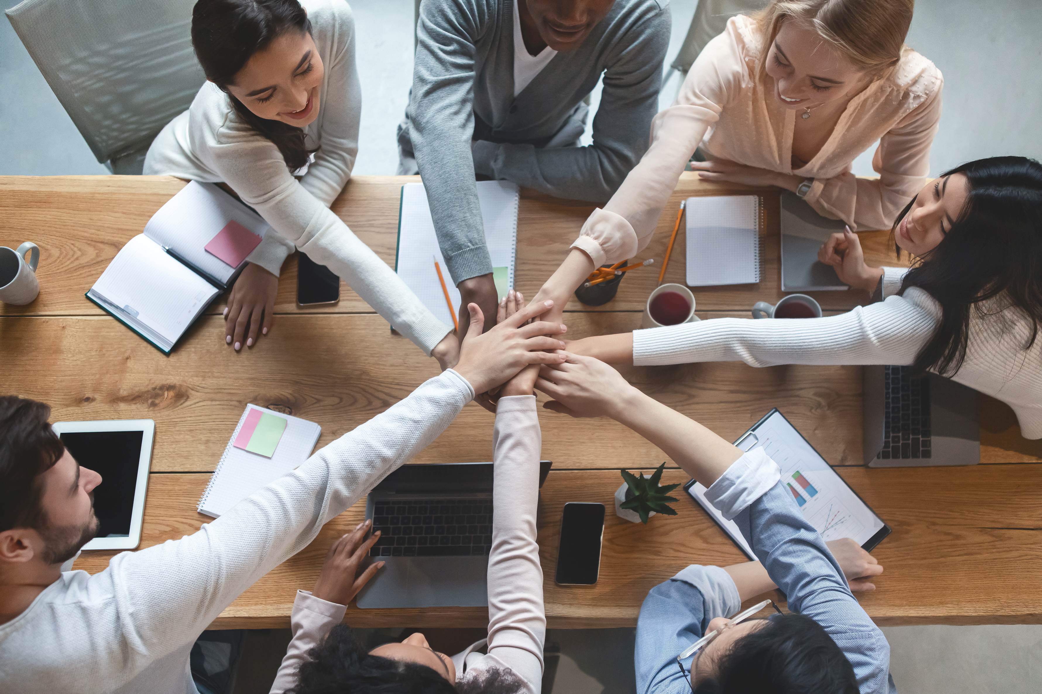 group of people around a table put their hands together as a gesture of teamwork in an office setting