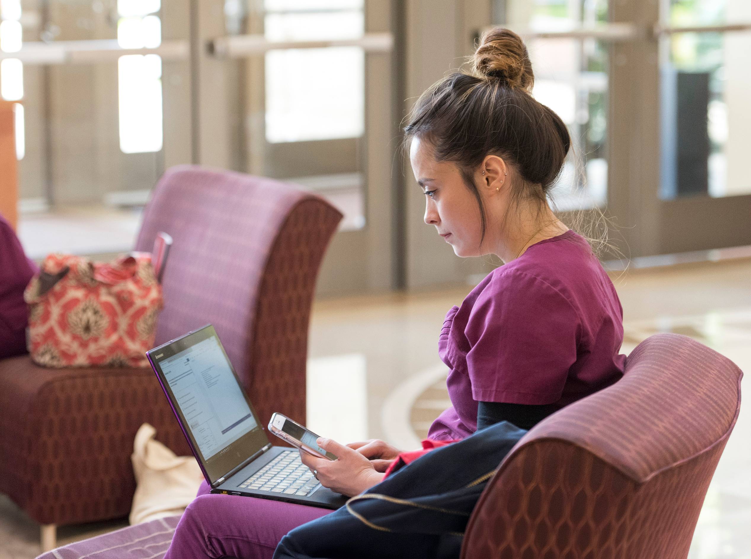 woman in scrubs sitting down in chair and looking at a laptop