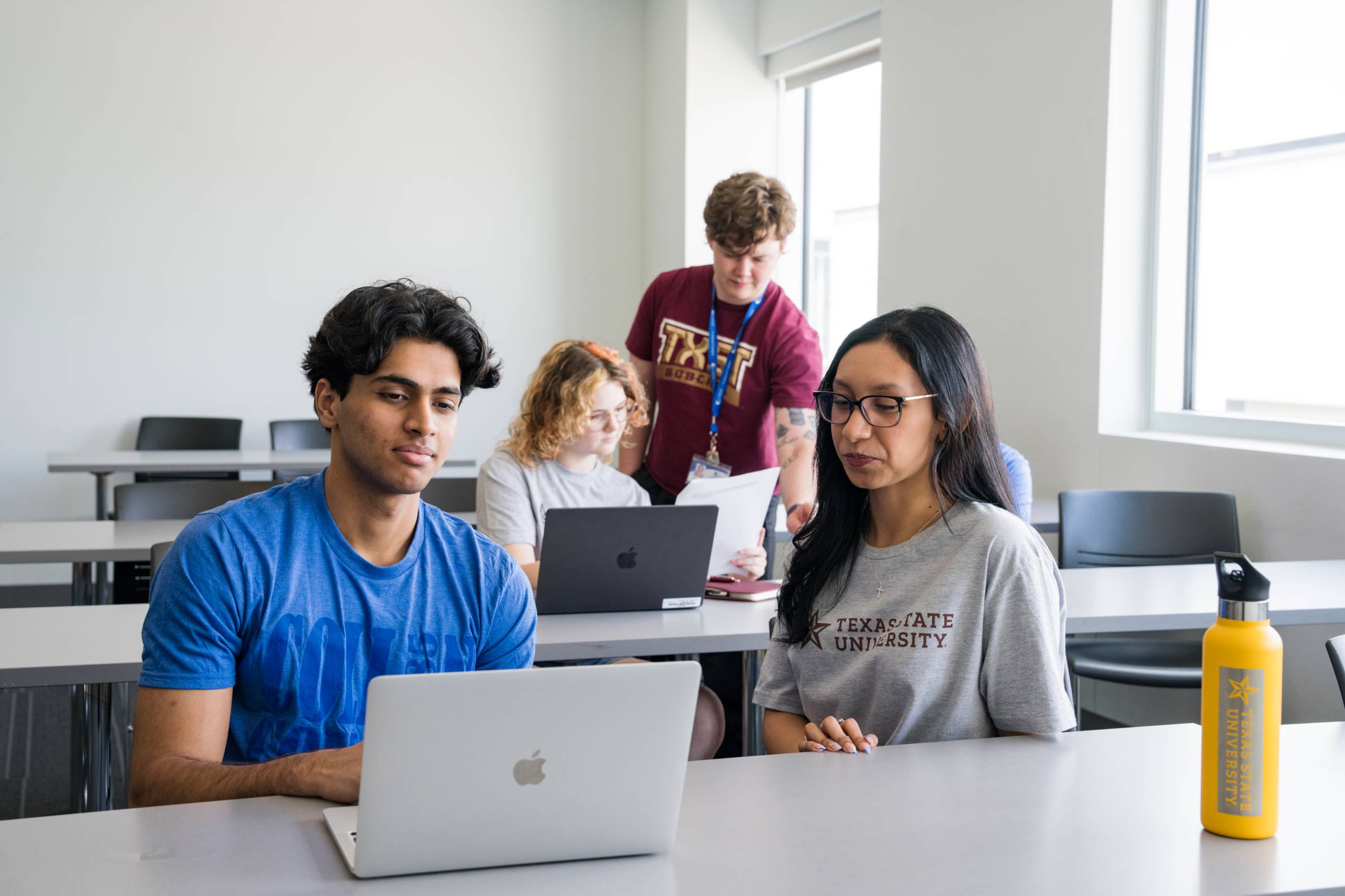 students look at a laptop while an instructor helps them