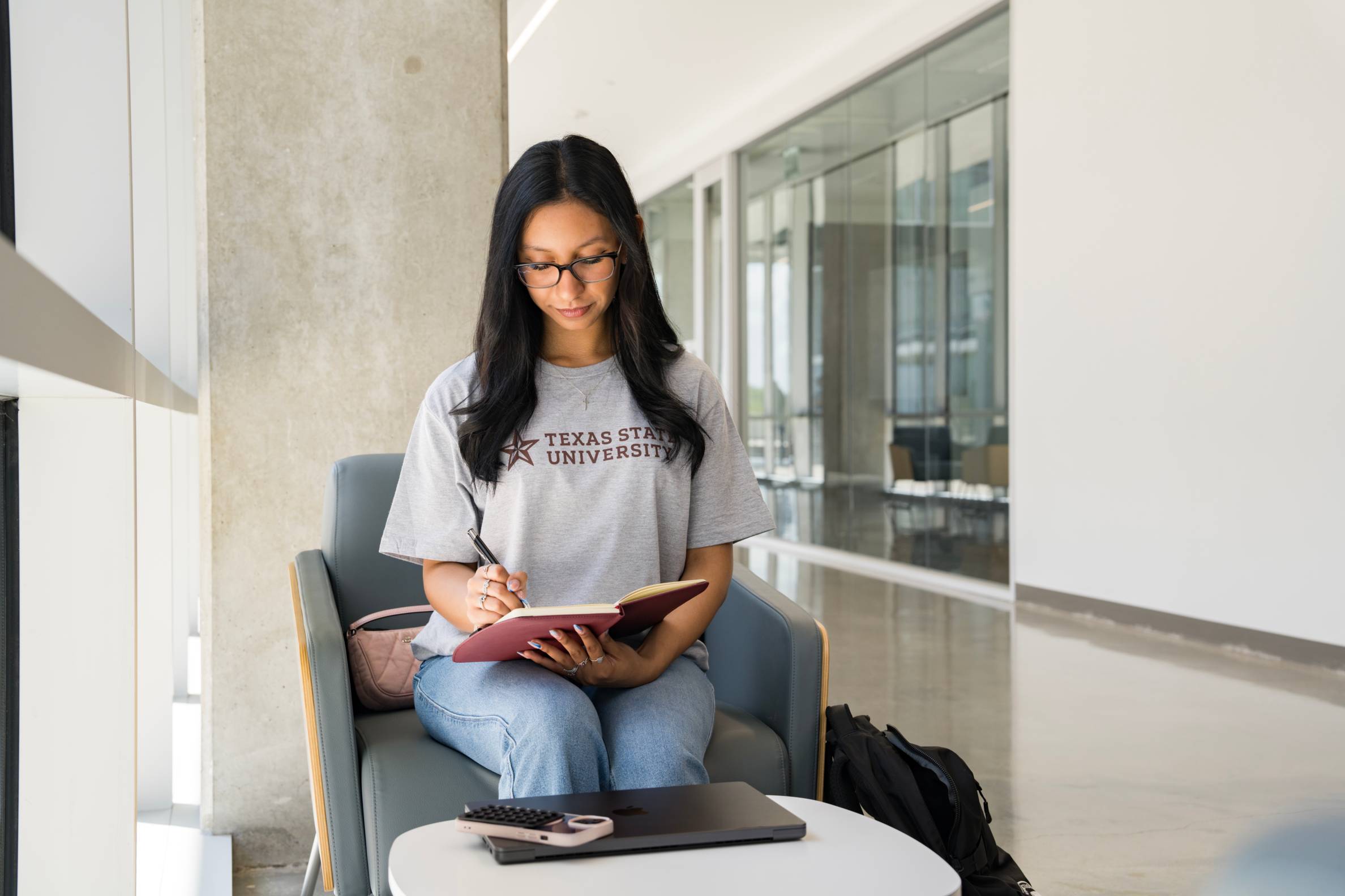 a TXST student writes in a notebook near well-lit window