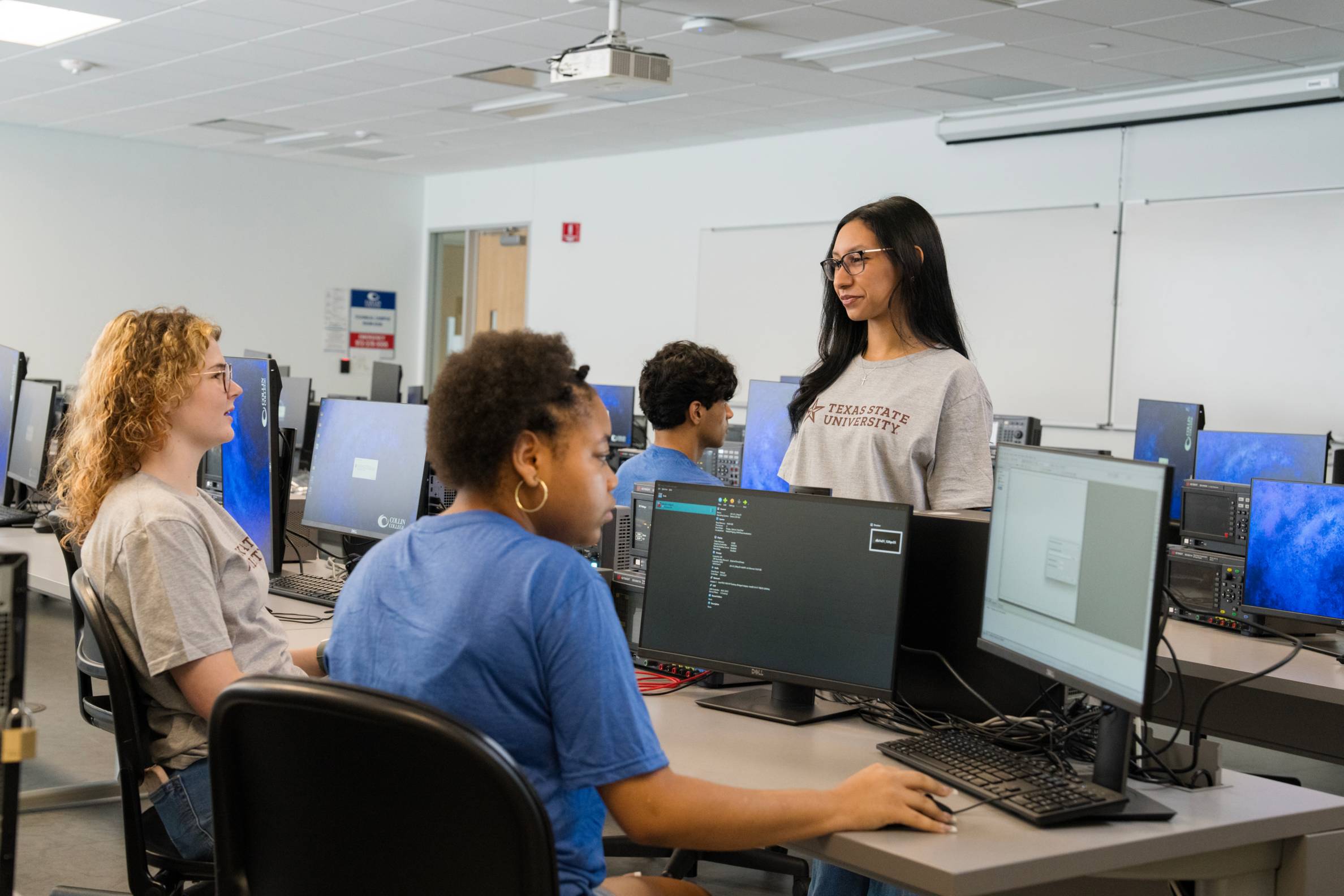 a group of students gather around electrical devices and computers