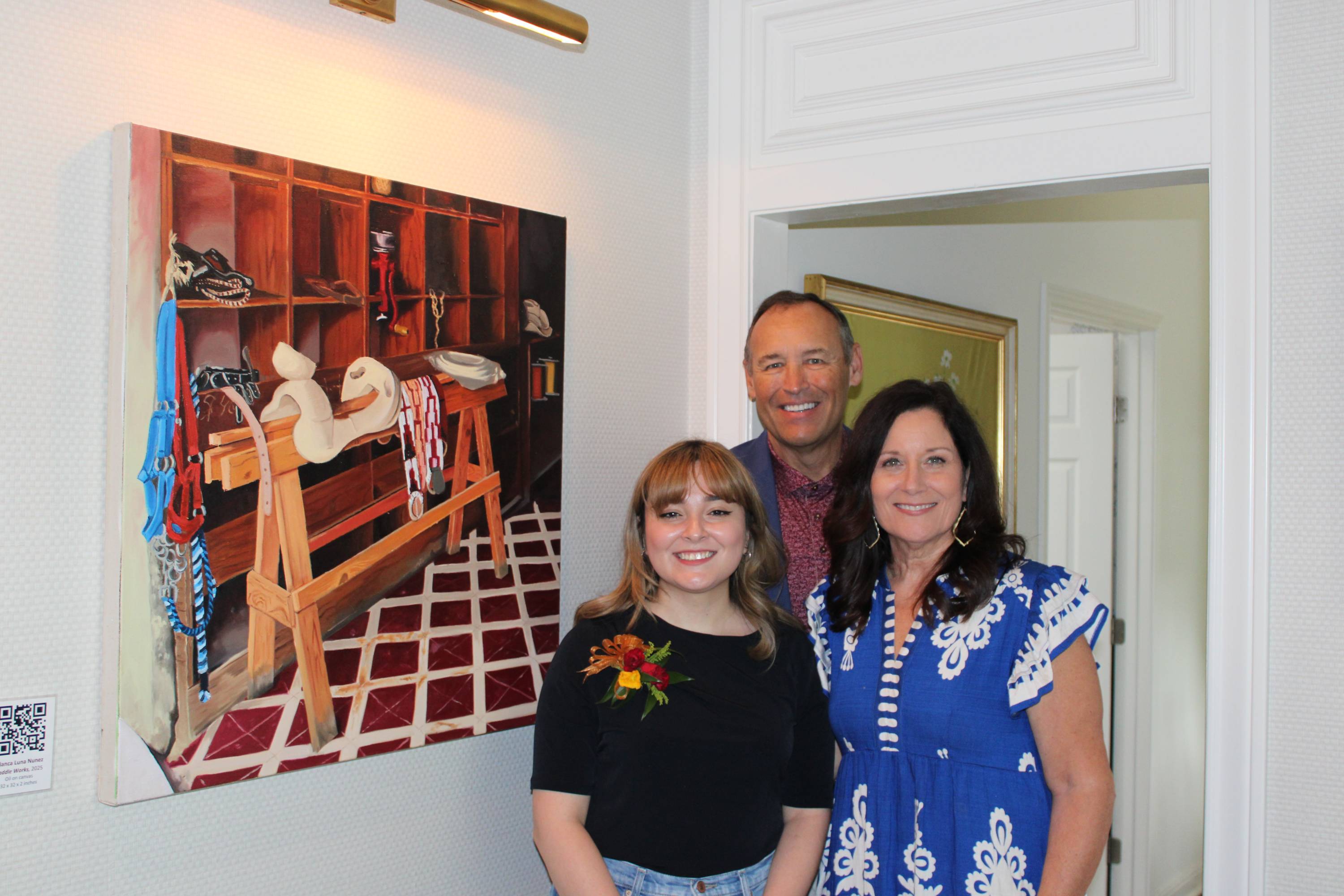 two women and a man stand next to a color acrlyic painting of a saddle