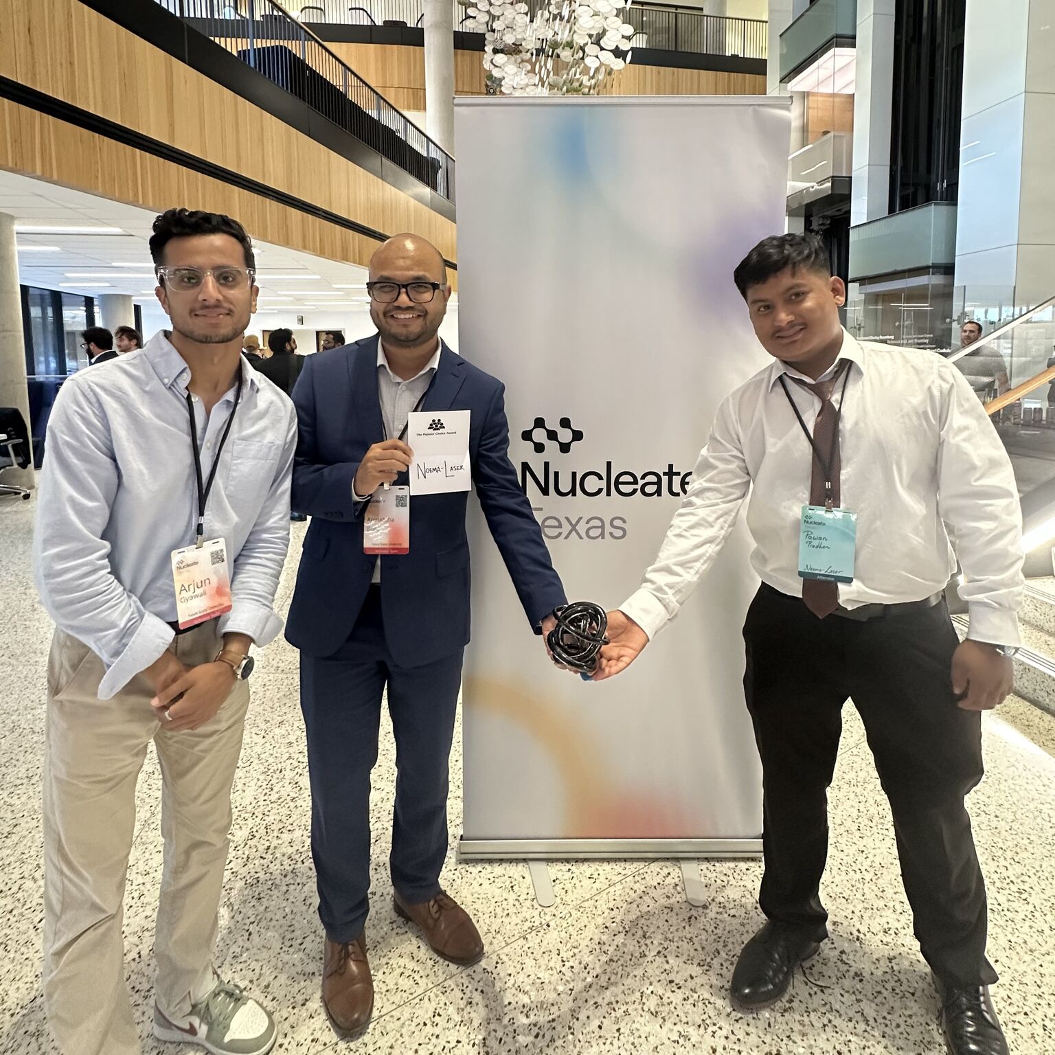 three men posing for photo in front of sign reading "nucleate"