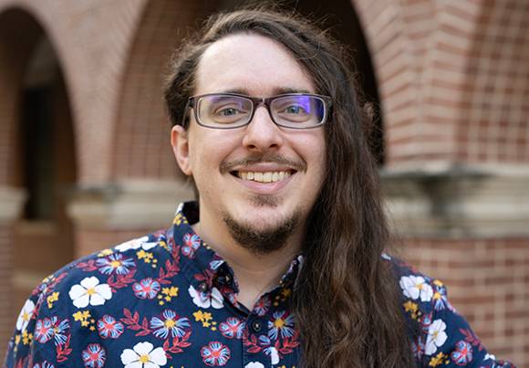 Photo of Jonathan Vontsteen. he has long curly dark hair. black rectangle glasses. and a blue flower print shirt
