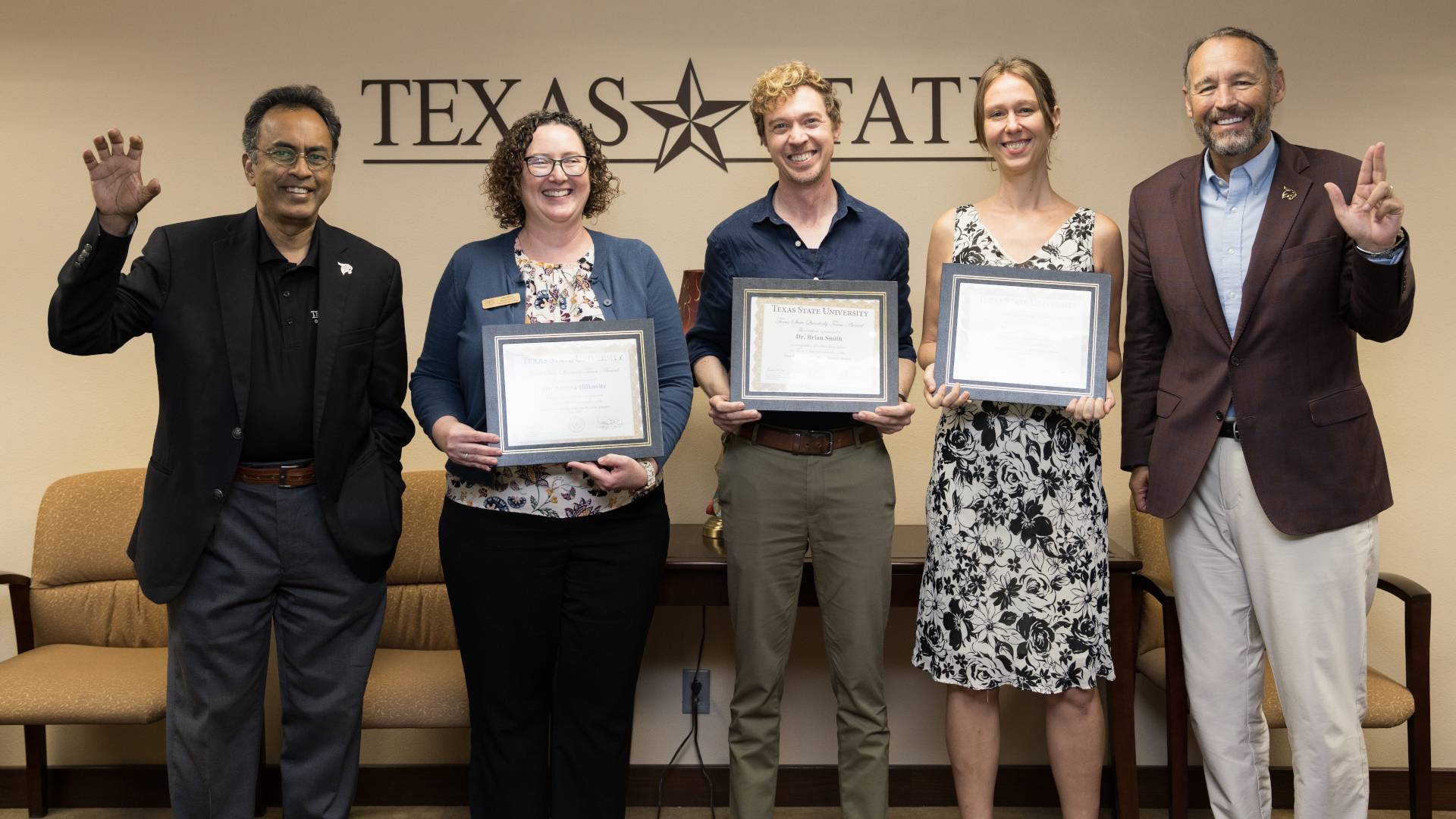 two women holding awards, one man holding an award, flanked by one man making the "eat 'em up, cats!" gesture, and another making the TXST hand gesture