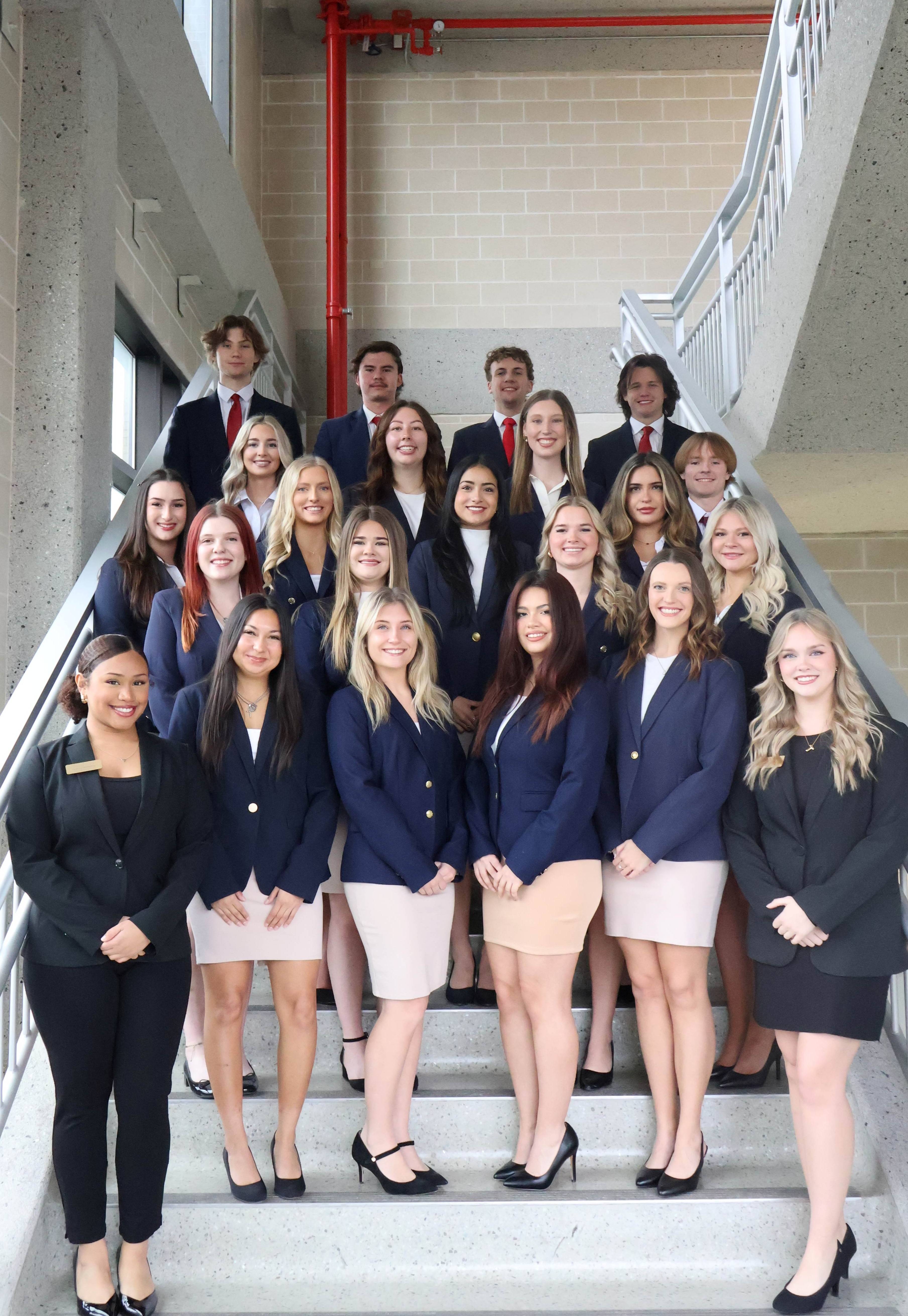 Group of Sales Ambassadors standing on the stair case in khaki bottoms and navy blue suits.