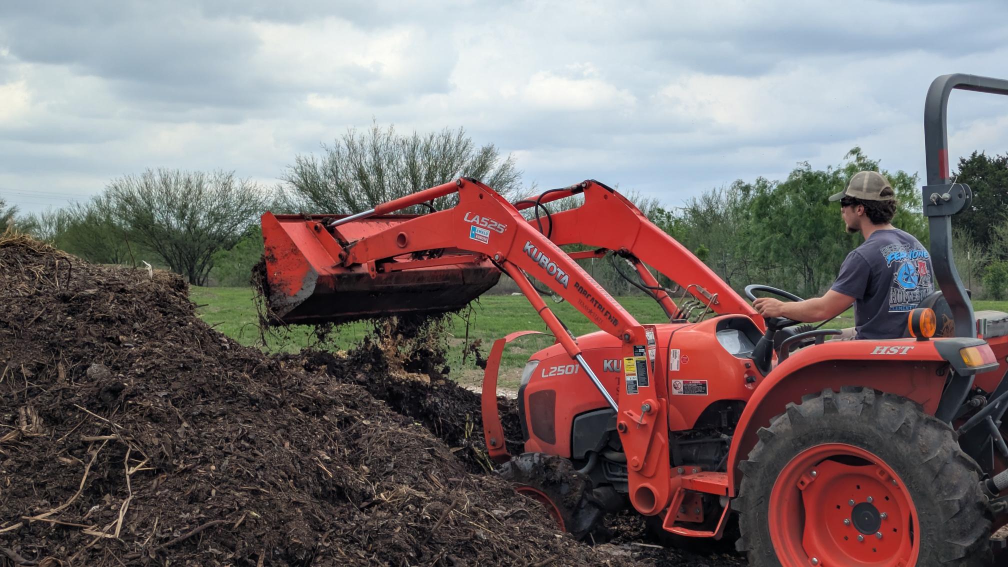 An orange tractor in a large compost pile.