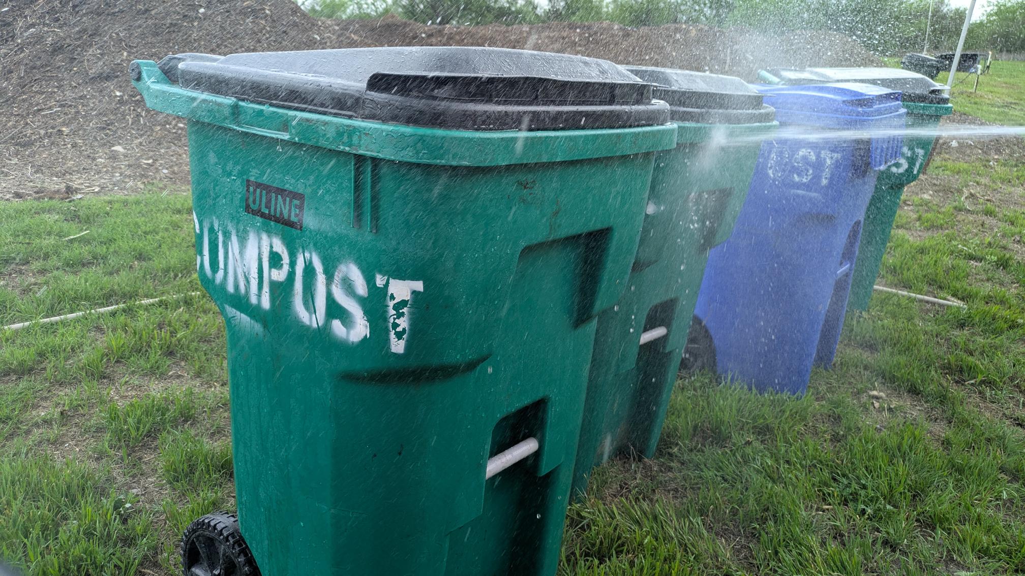 A trash can labelled "compost" being sprayed with water.
