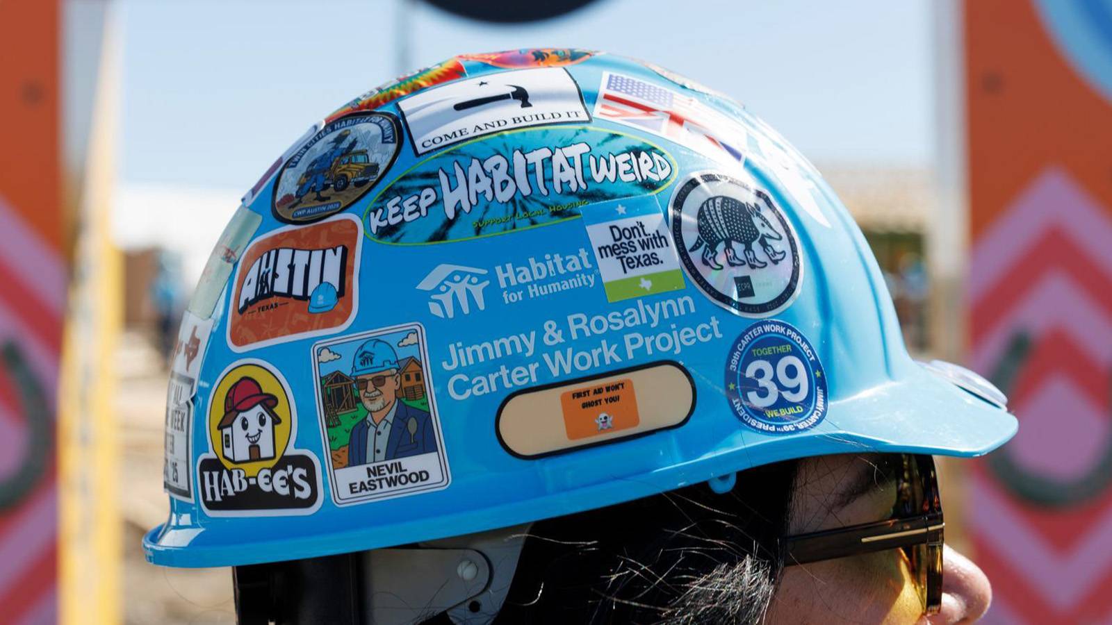 close up of woman wearing a hard hat covered in various stickers with a blurred background