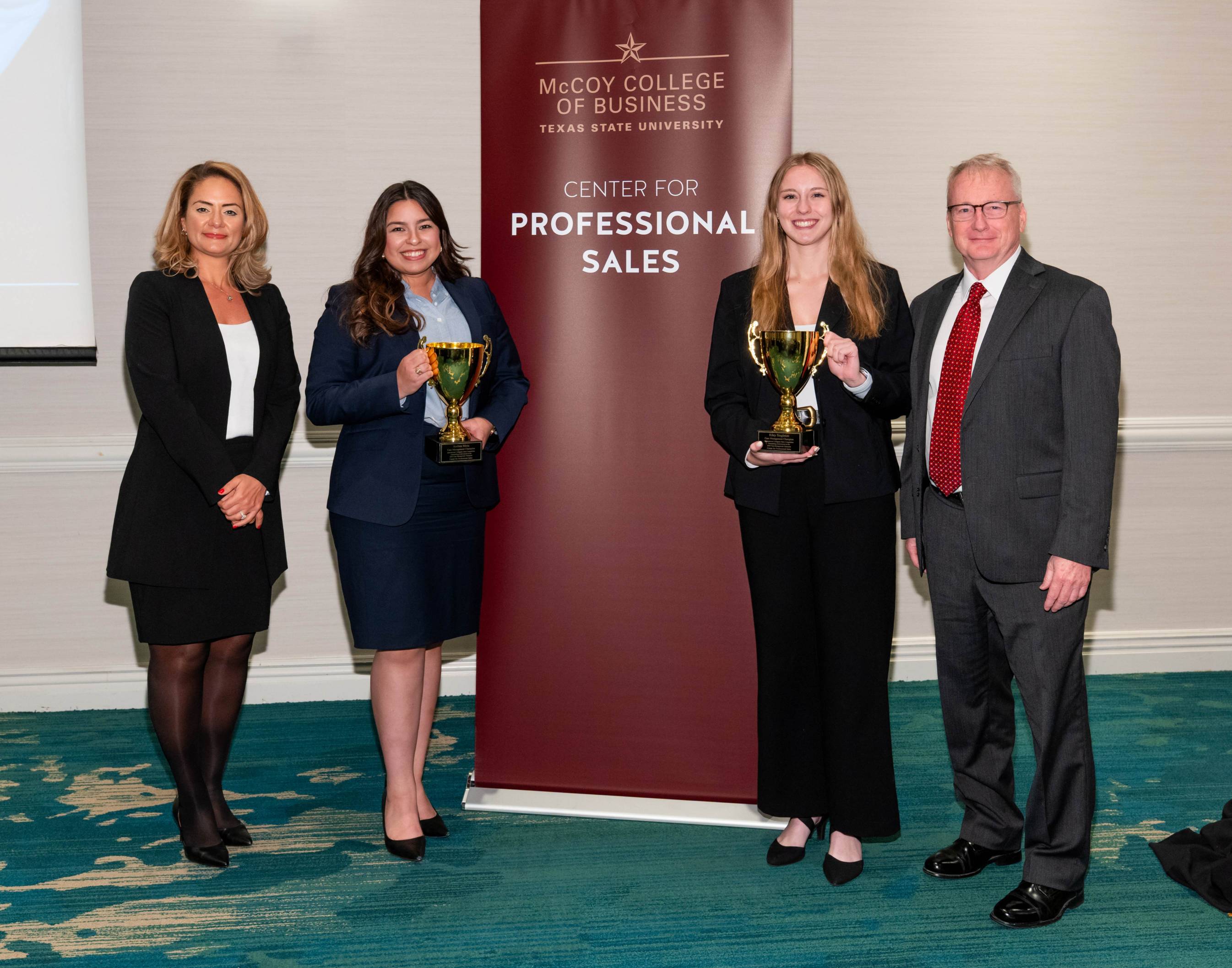 two students holding gold trophies with two professors