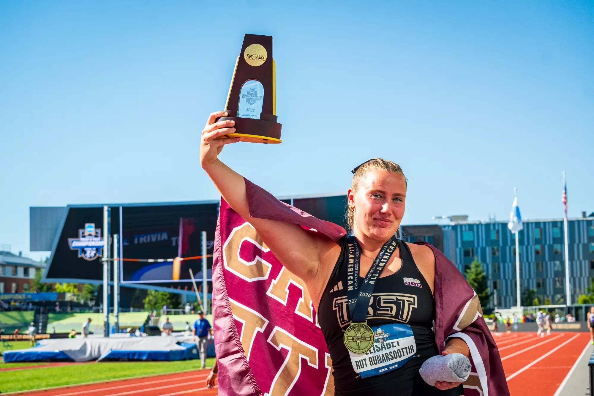 Outdoor track athlete poses for a photo with her medal and trophy at the NCAA Outdoor Championship.