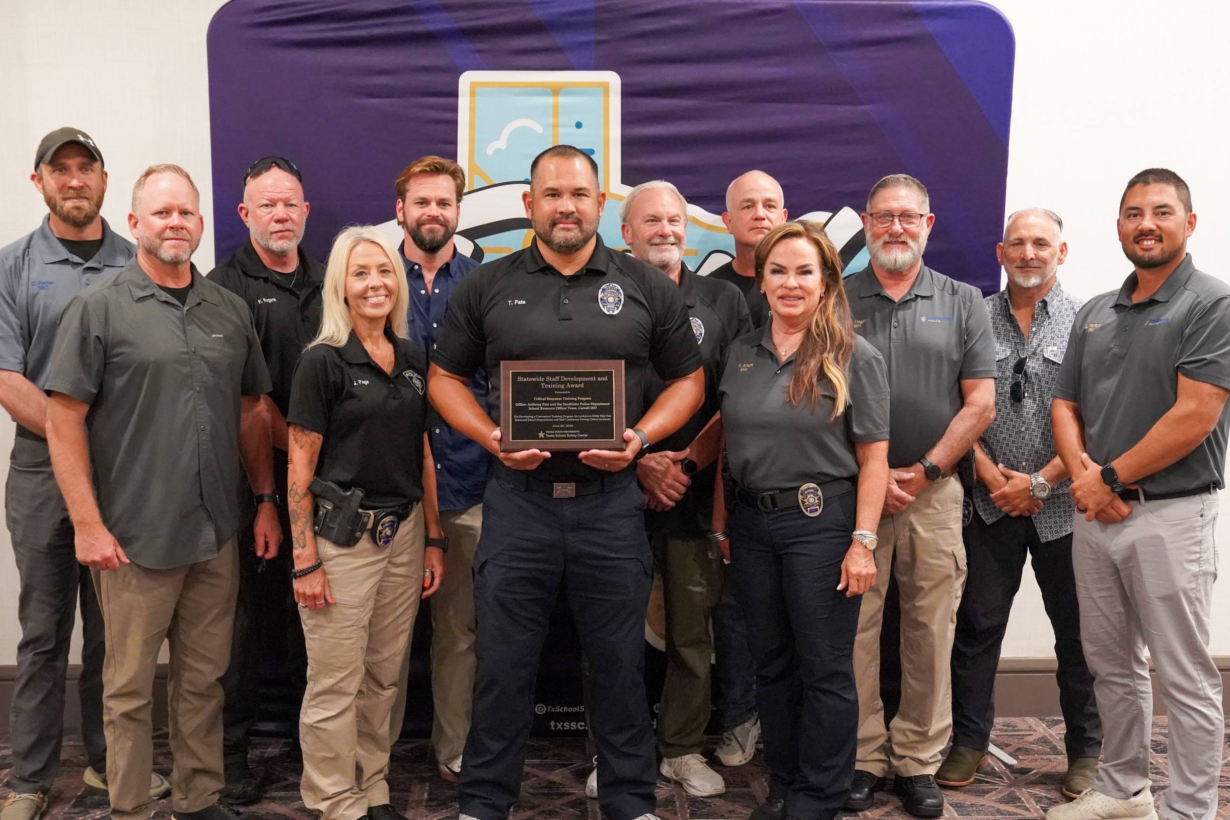 large group of people in grey shirts and khaki pants pose with award plaque