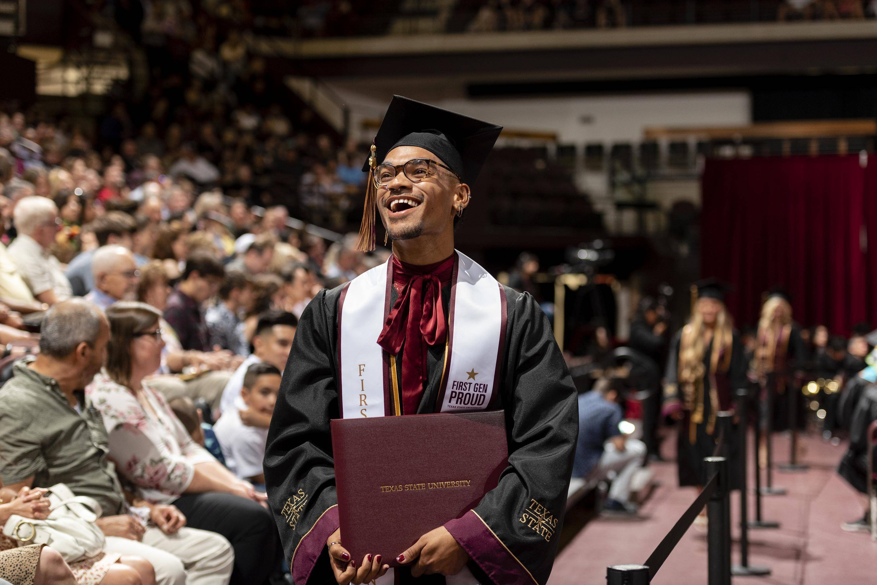 male graduate smiles at crowd during graduation ceremony. 