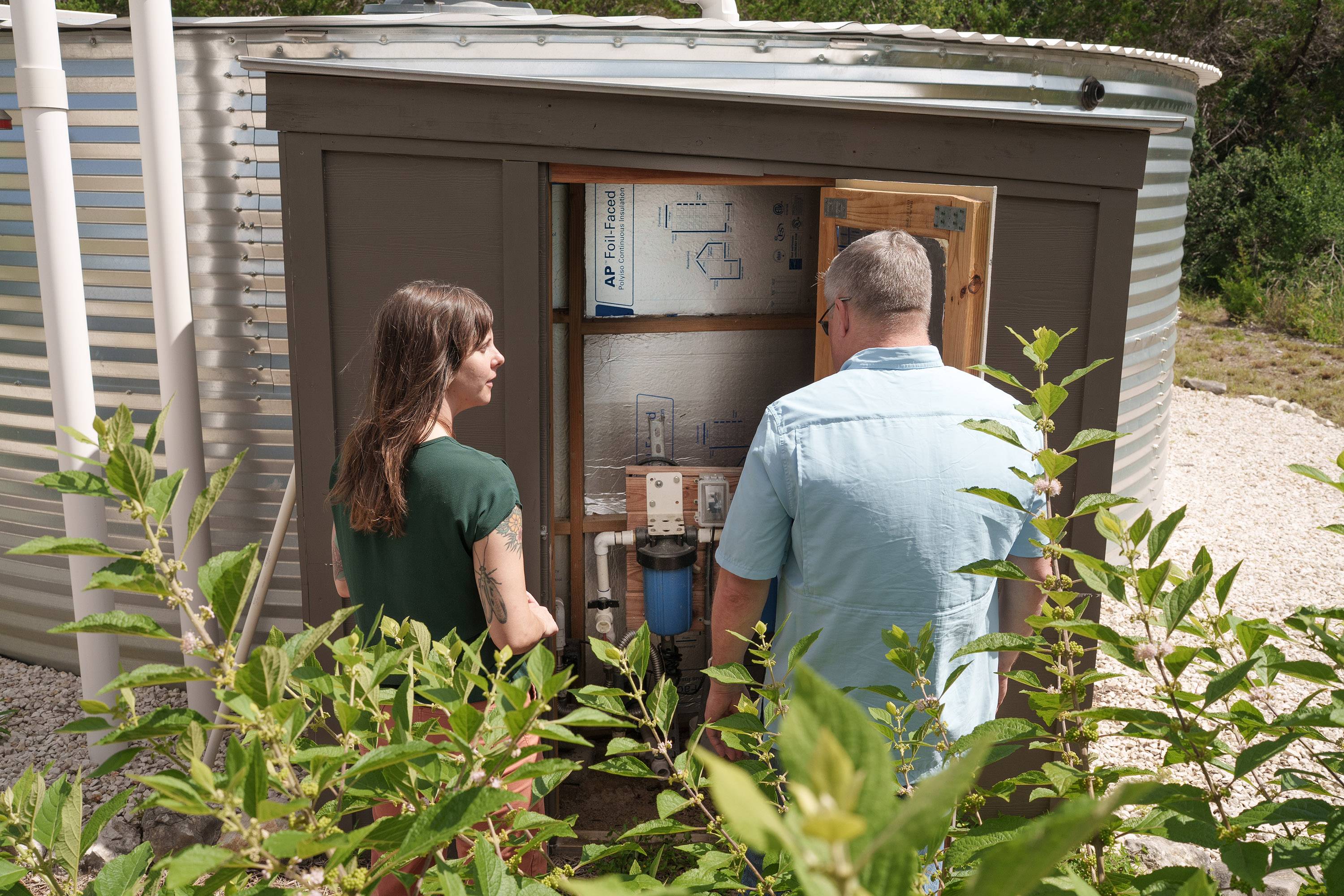 Dr. Robert Mace and Katie Tritsch look at the filtration system in a shed next to the water tank.