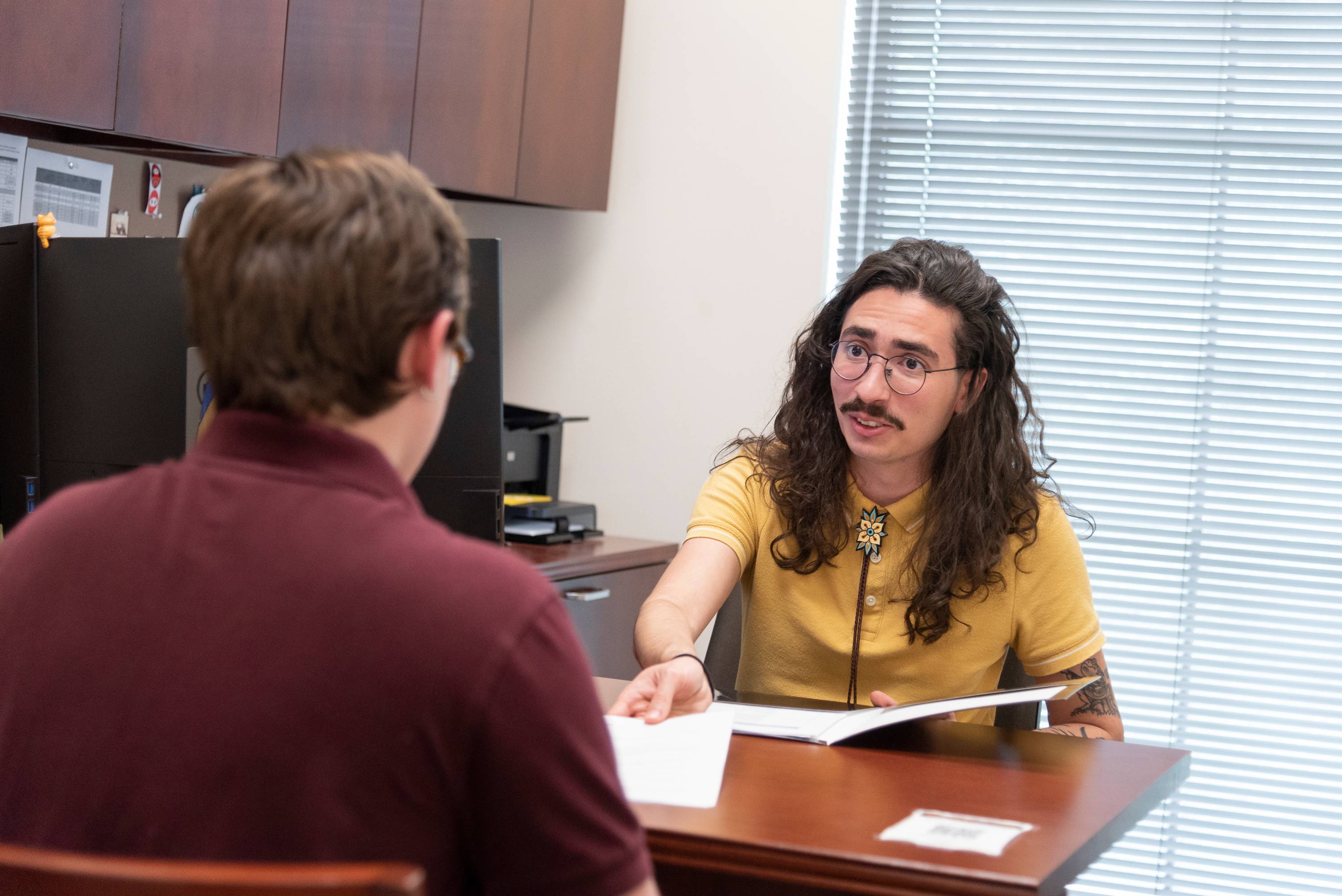 An advisor sits across a desk from a student having a conversation.