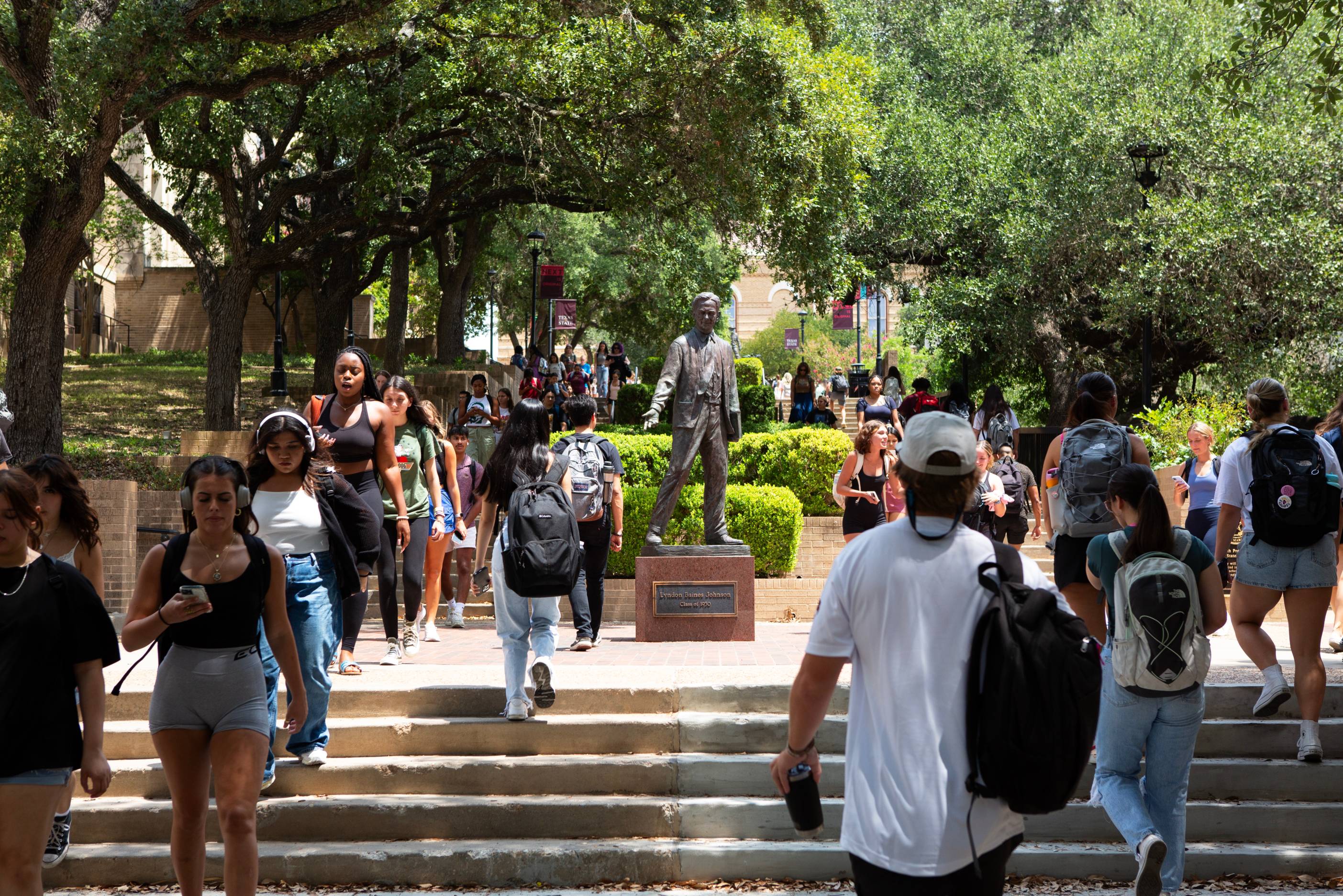 Students walk up and down outdoor stairs around a statue of young Lyndon Baines Johnson. 