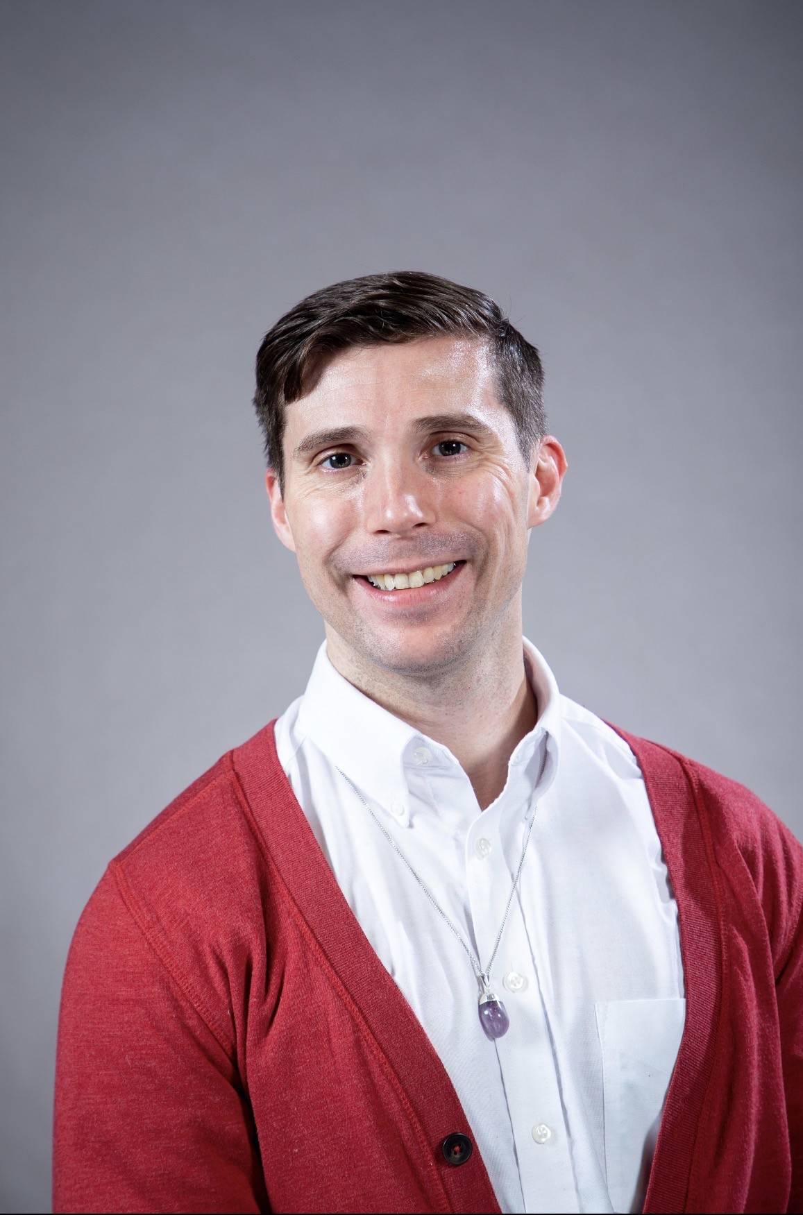 man wearing red sweater, white oxford shirt, chain with pendant, grey background