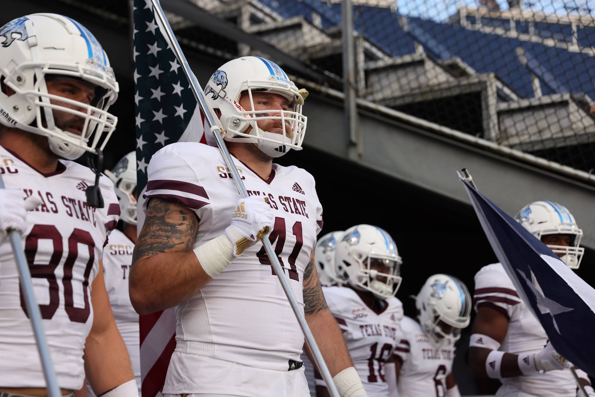 football player in white uniform and helmet carrying an american flag