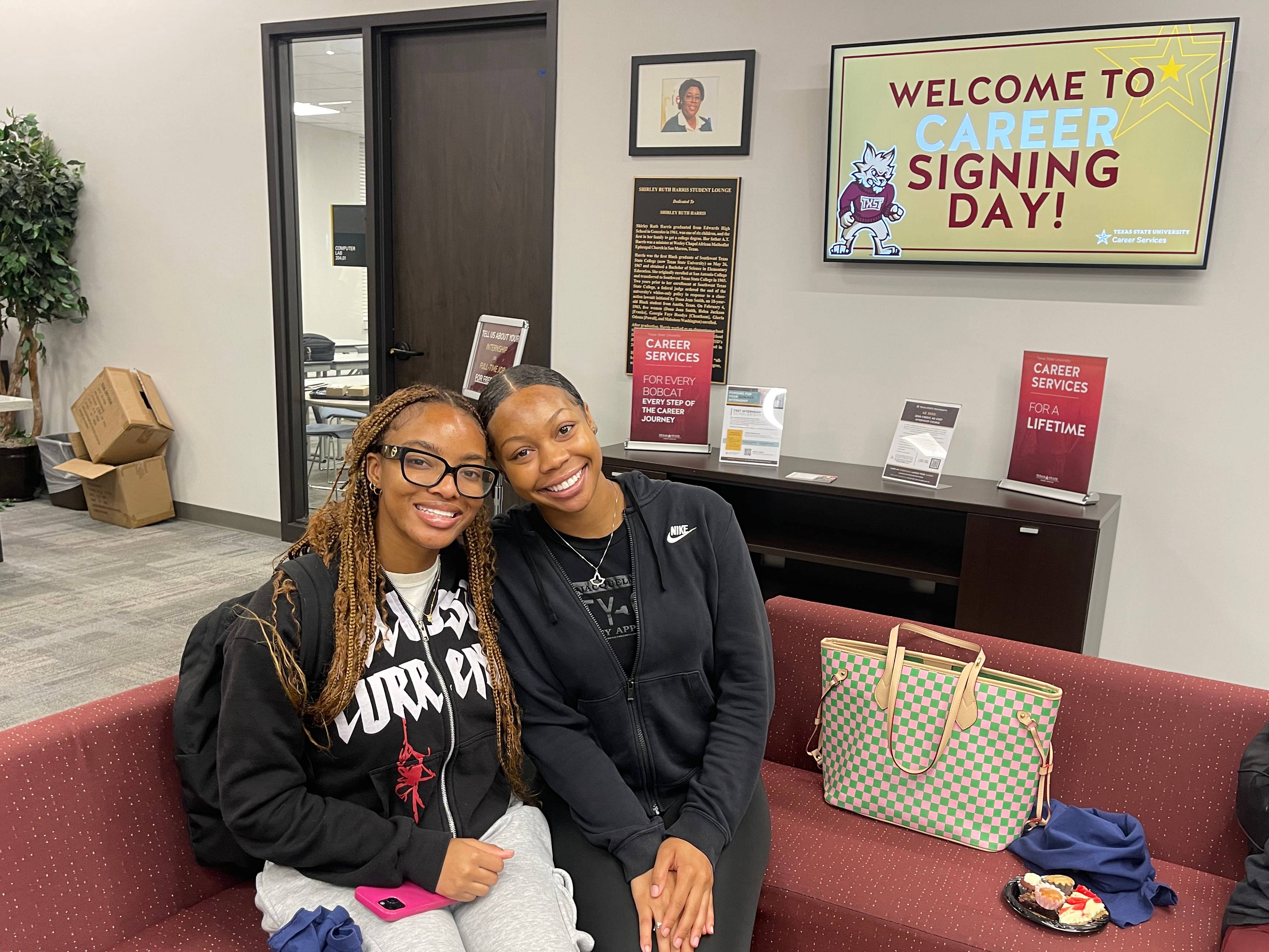 two women sitting in lounge next to sign reading "Welcome to Signing Day!"