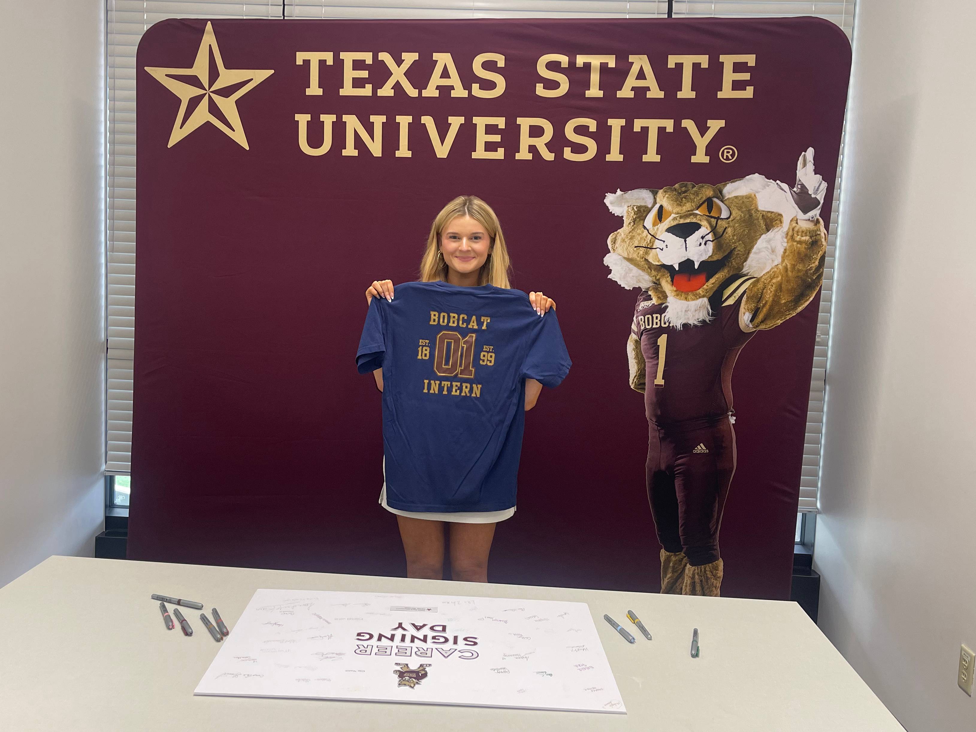 woman holding up shirt that reads "Bobcat Intern"