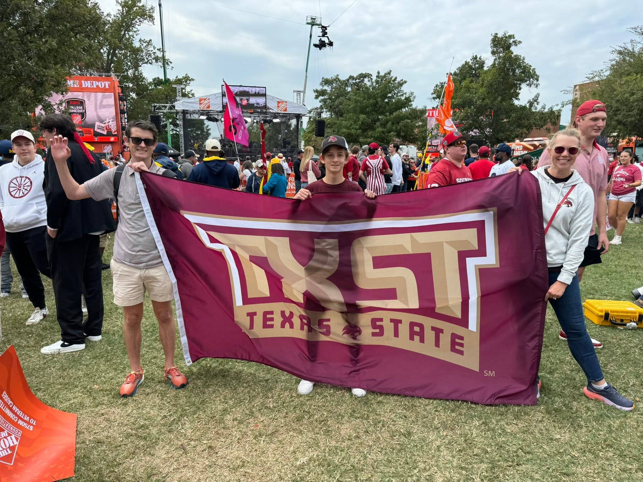 Two Texas State alum and a young Texas State fan holding up a Texas State flag