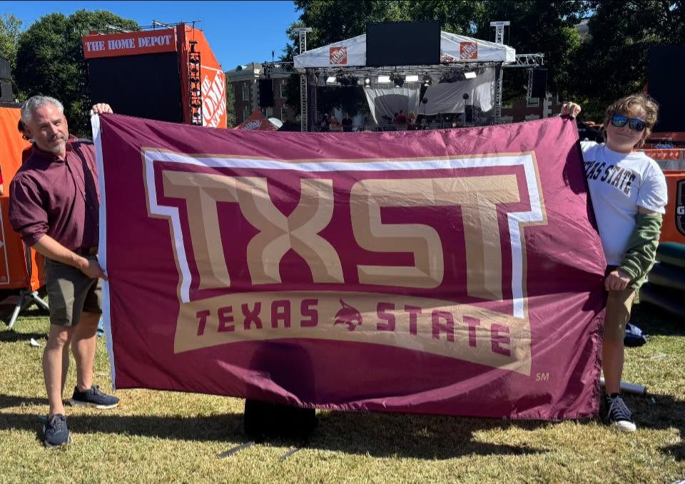 A Texas State alum and young Texas State fan holding up a Texas State flag